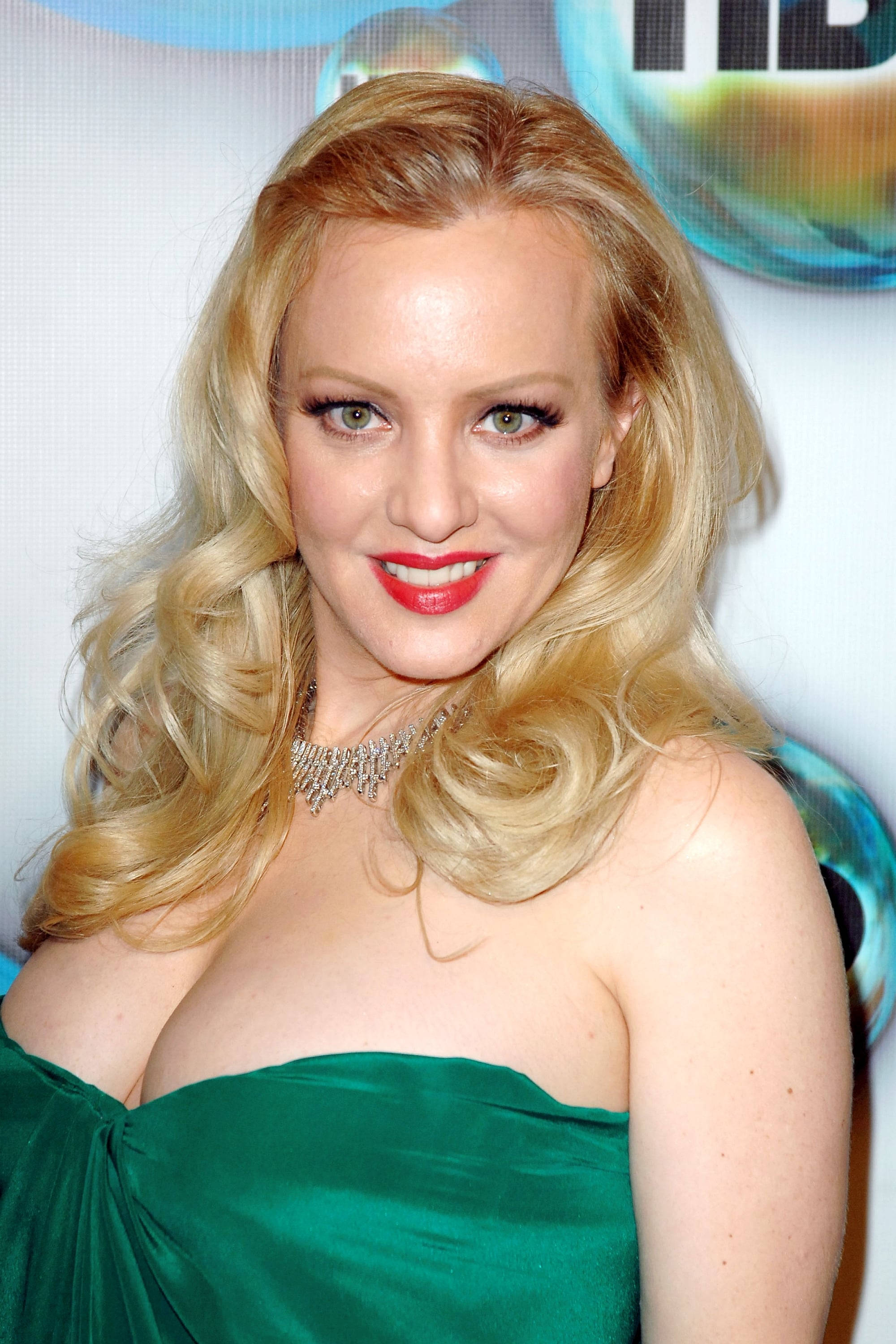 Celebrity 桌布 壁紙 — 一位金髮美女穿著綠色無肩帶連衣裙，塗著大膽的紅色唇膏，戴著閃閃發光的鑽石項鍊，對著鏡頭微笑。