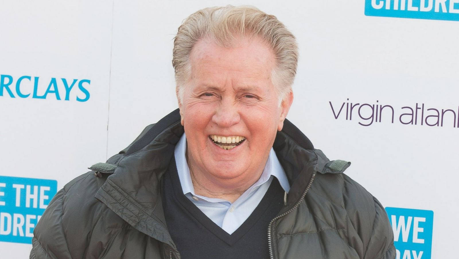 actor 桌布 壁紙 — 一位金髮老男人在品牌活動背景前穿著深色羽絨外套露出燦爛笑容。