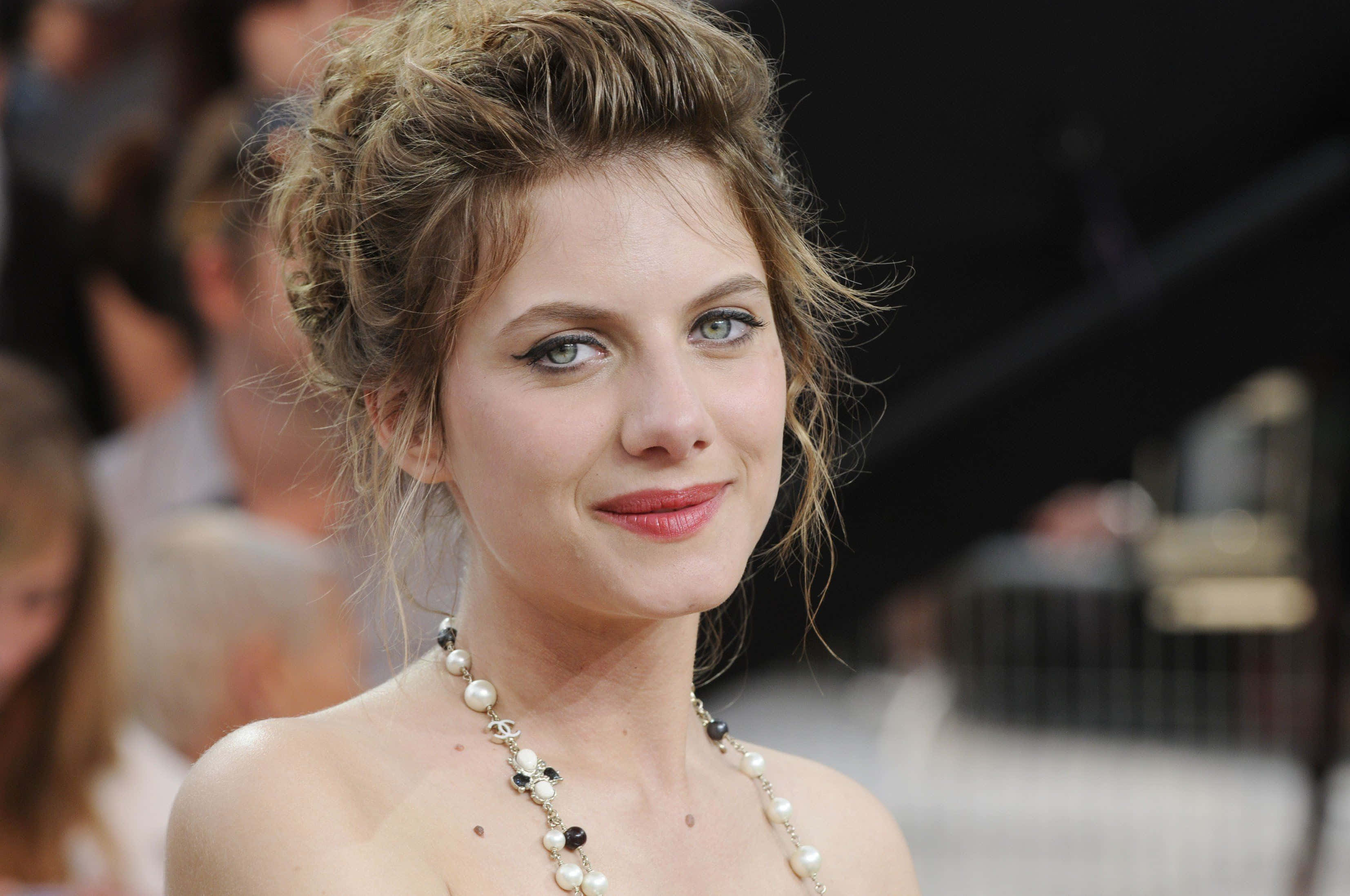 Mélanie Laurent 桌布 壁紙 — 一位金髮蓬鬆、戴著珍珠項鍊的女性近距離肖像，對著鏡頭溫柔微笑。