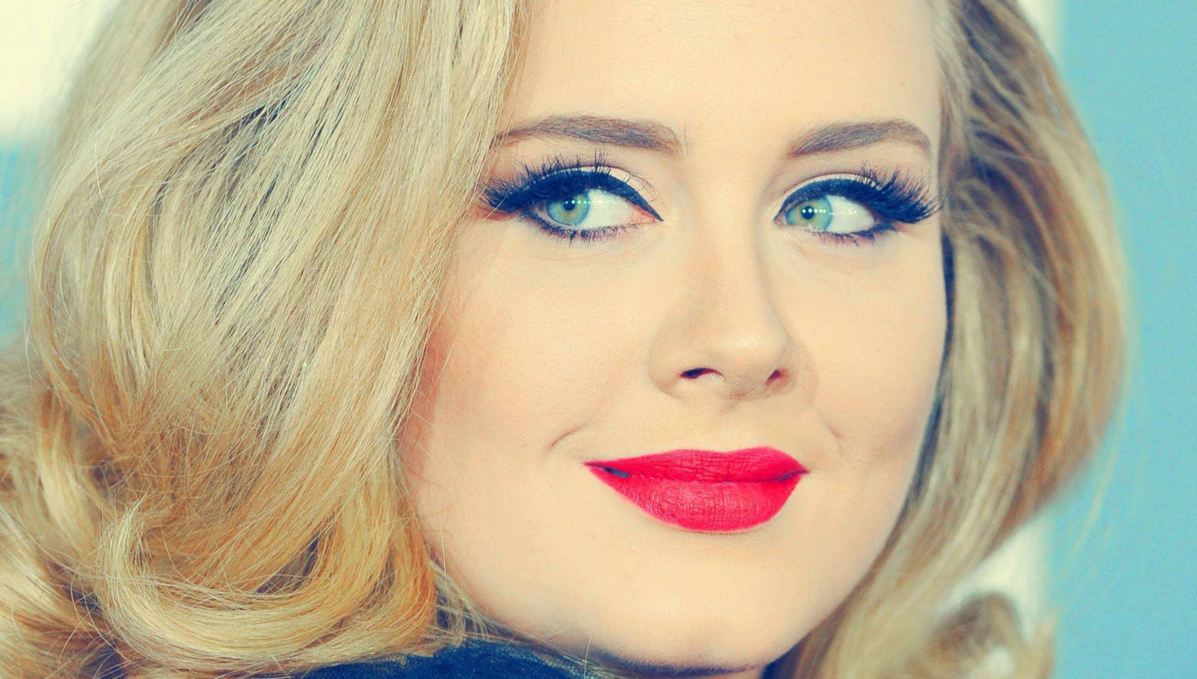 Adele 桌布 壁紙 — 一位金髮藍眼、塗著大膽紅唇膏的女性，在柔和的藍色背景前微笑的特寫肖像。