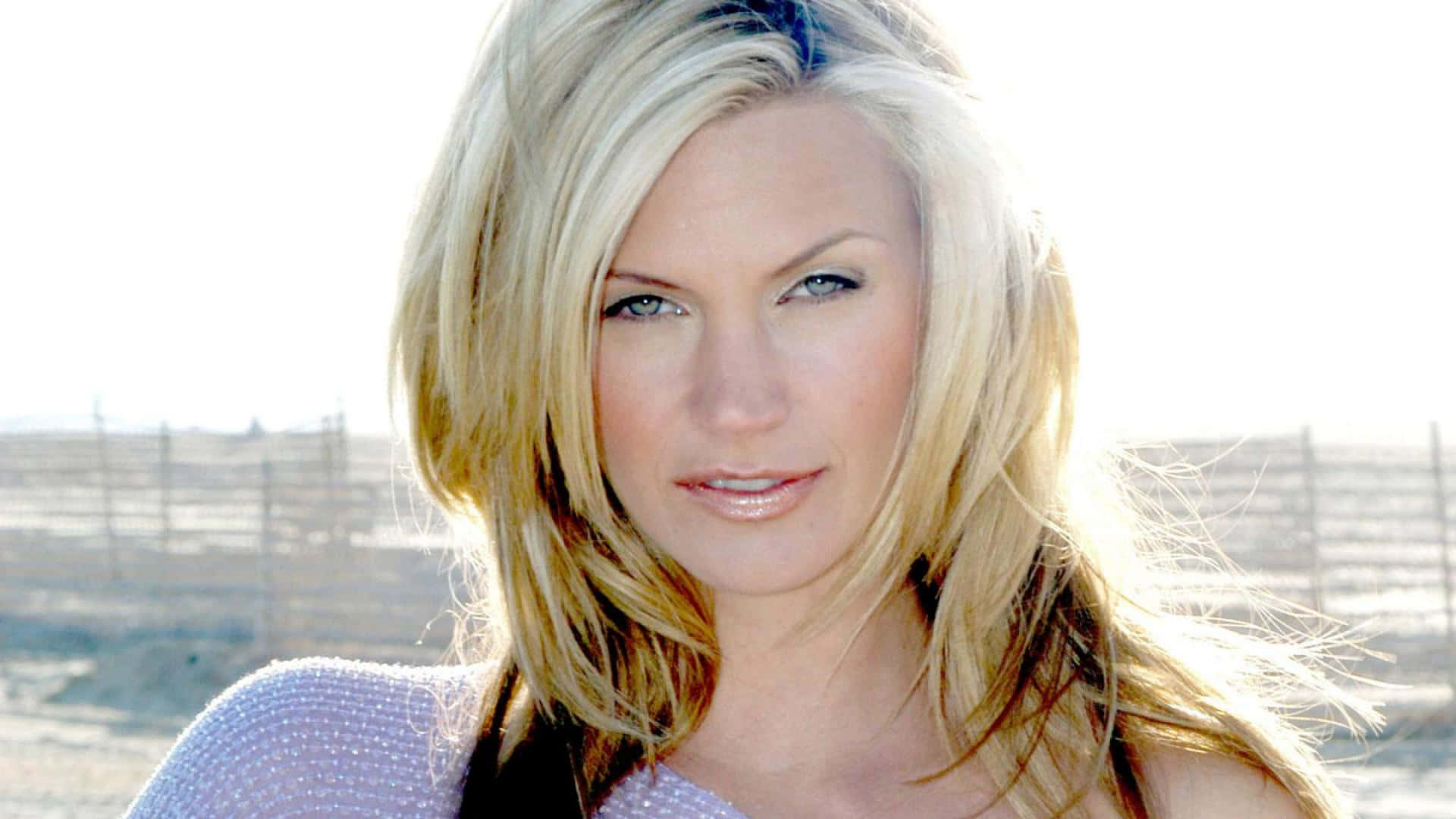 Natasha Henstridge 桌布 壁紙 — 一位金髮藍眼女士在明亮的戶外背景（有圍欄）下直視鏡頭。