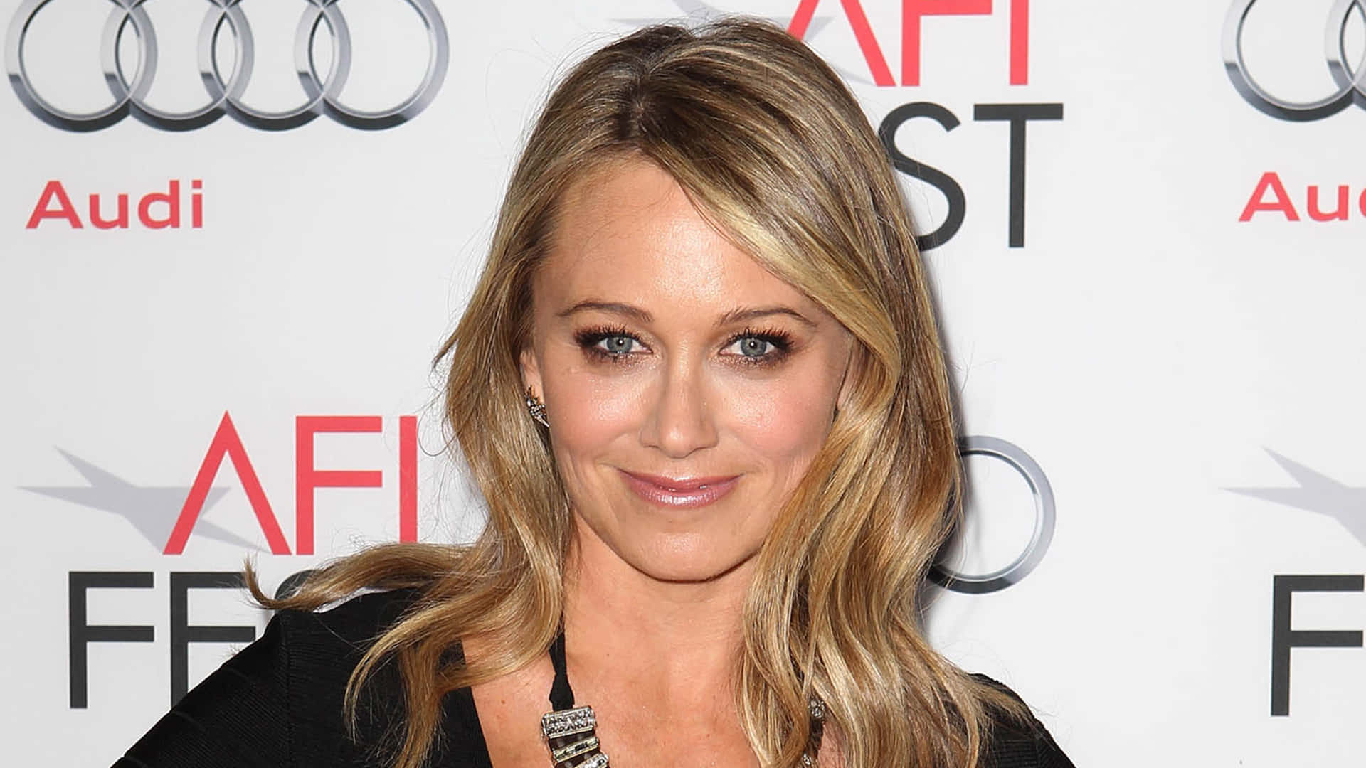 Christine Taylor 桌布 壁紙 — 一位金髮藍眼女士在白色背景前微笑，背景有Audi和AFI FEST標誌。