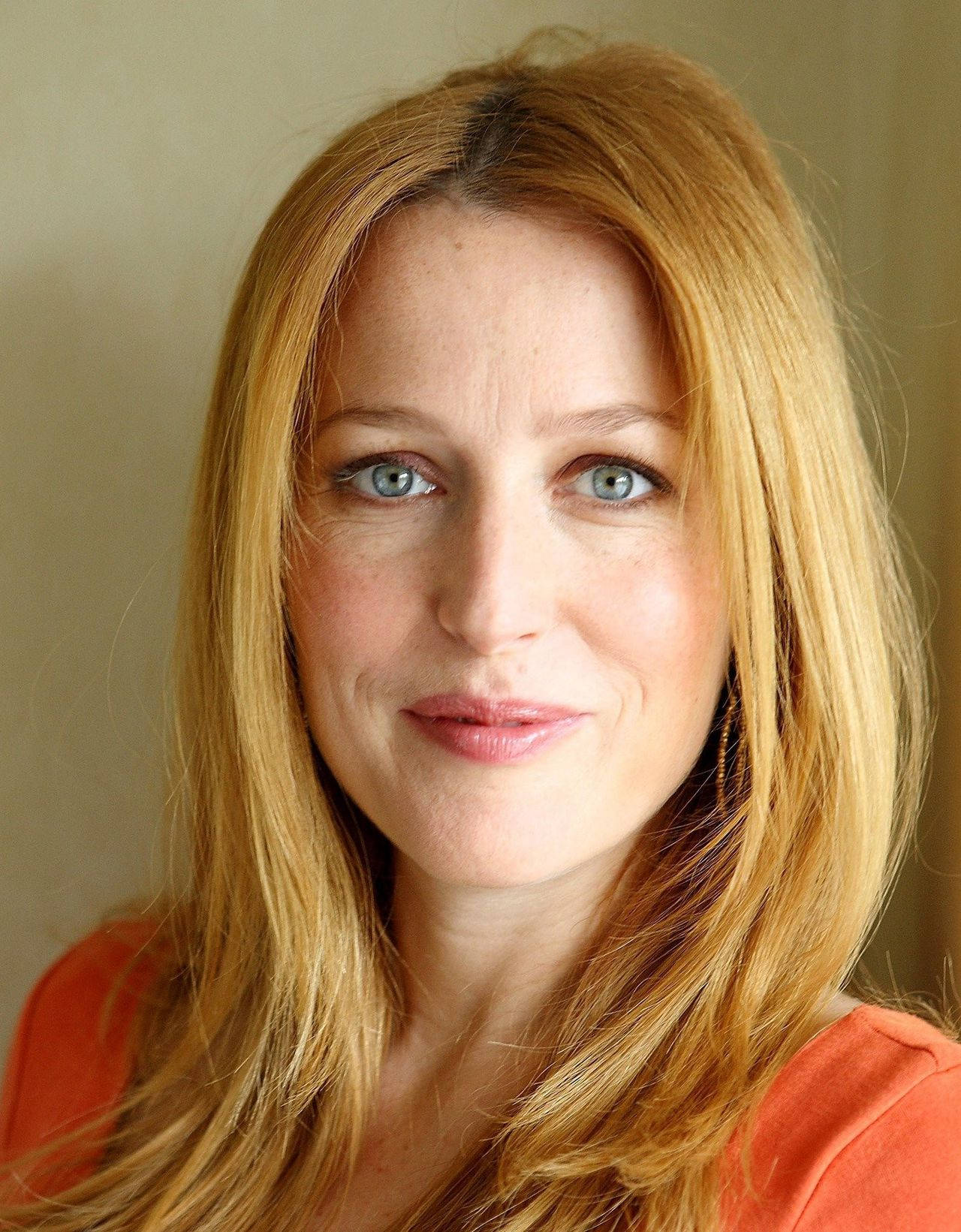 gillian anderson 桌布 壁紙 — 一位金髮藍眼女士在純色背景下微笑的特寫肖像。