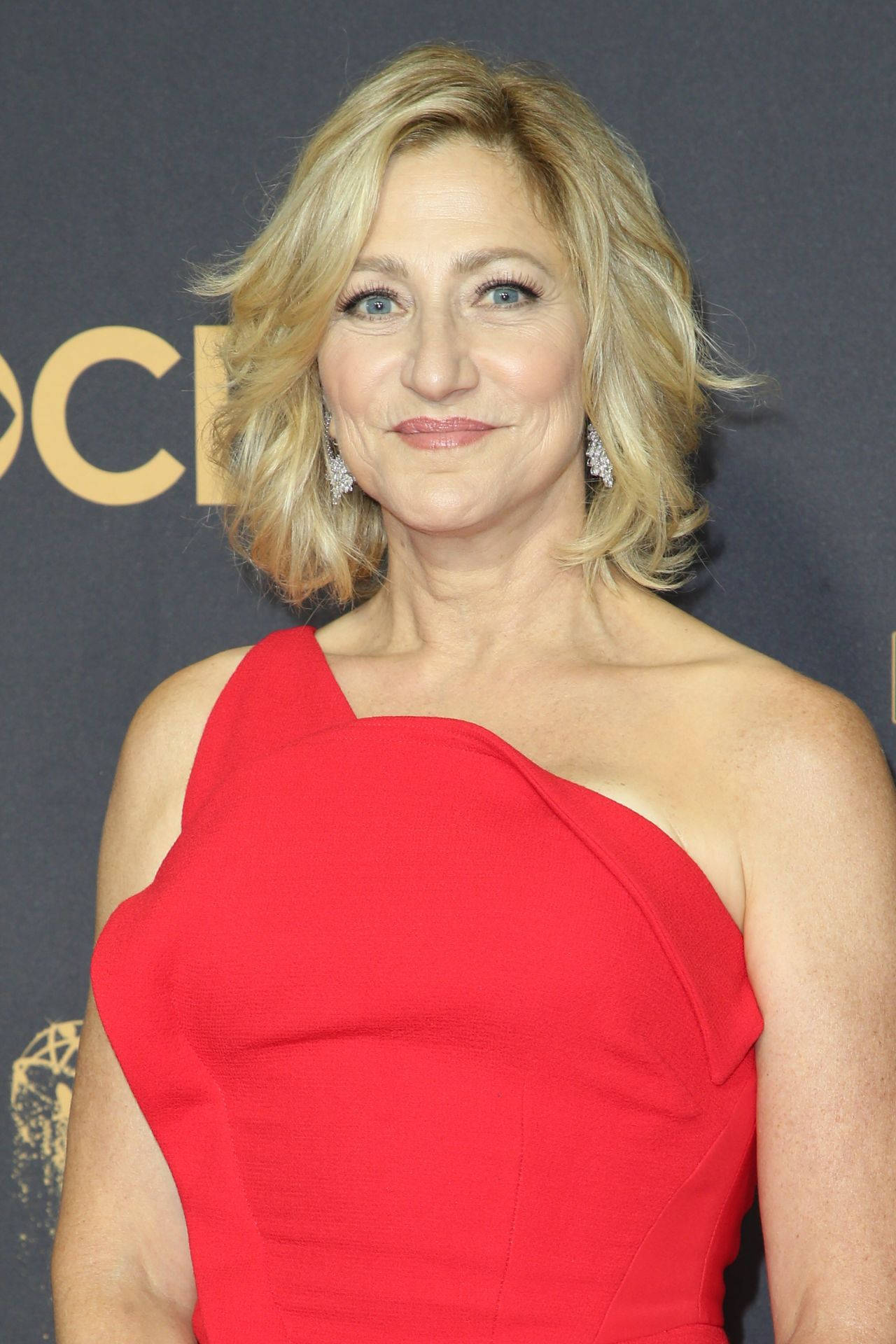 Celebrity 桌布 壁紙 — 一位金髮藍眼女士在頒獎典禮上穿著搶眼的紅色單肩裙微笑。