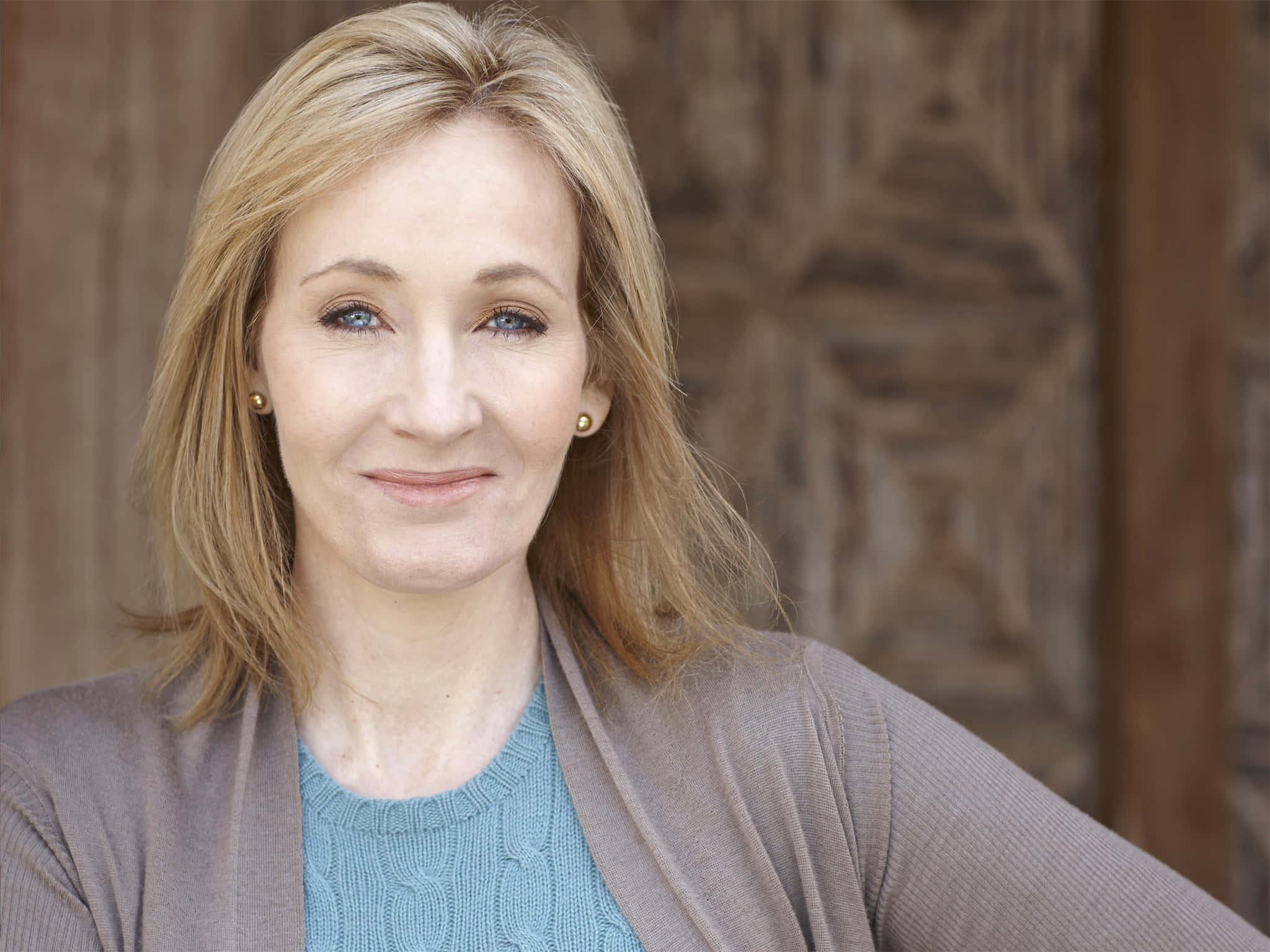 J K Rowling 桌布 壁紙 — 一位金髮藍眼的女士在紋理木質背景前溫柔微笑。
