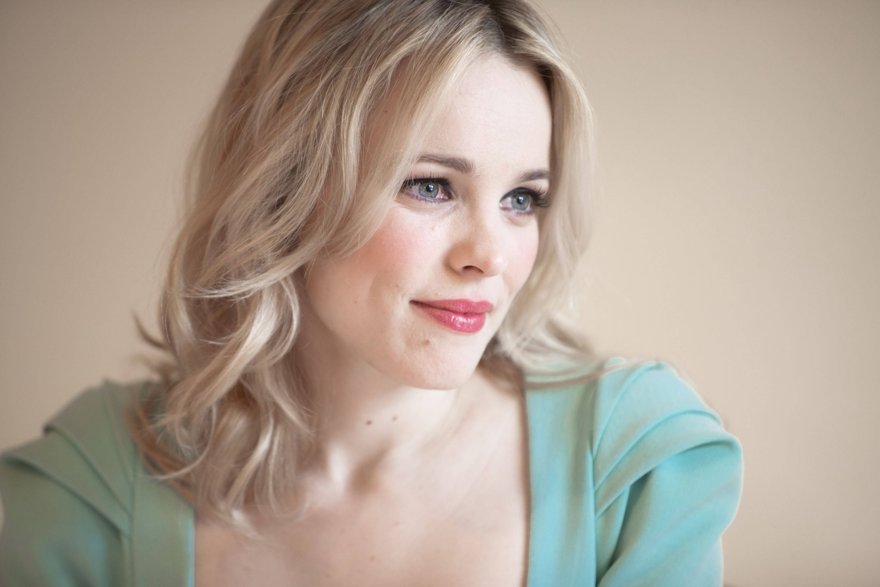 Rachel Mcadams 桌布 壁紙 — 一位金髮藍眼的女性，身穿青綠色上衣，在米色背景前溫柔微笑。