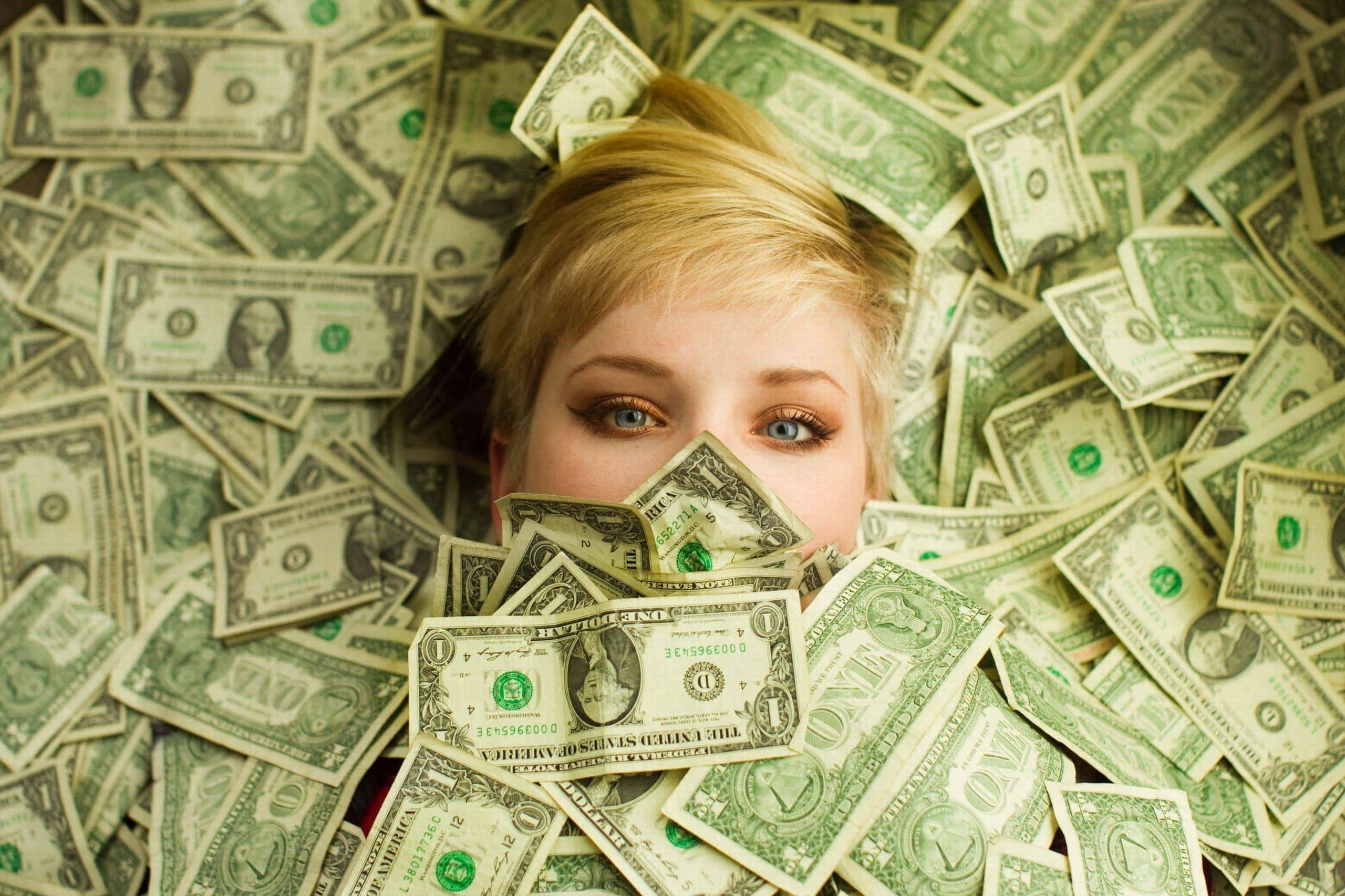 dollar 桌布 壁紙 — 一位金髮藍眼的年輕女子躺在散落的一美元鈔票中，她的臉部分被現金遮蓋。