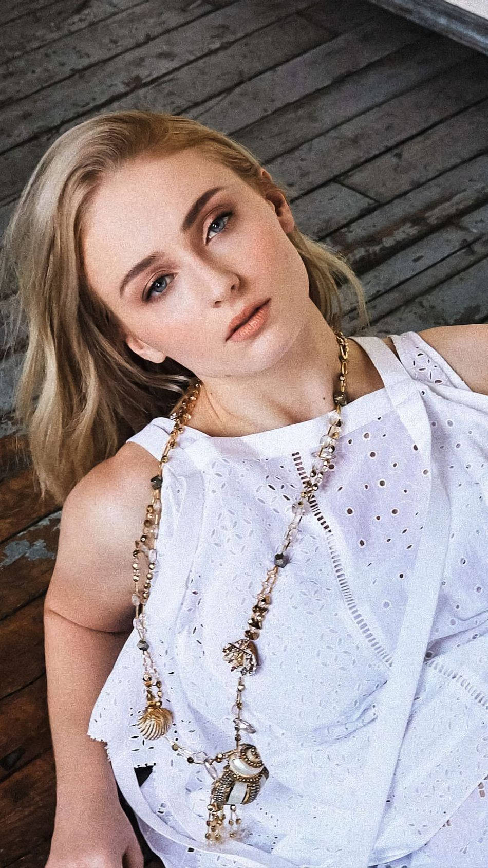 Sophie 桌布 壁紙 — 一位金髮藍眼的年輕女性，身穿白色鏤空上衣和華麗的金項鍊，在風化的木地板上仰望。