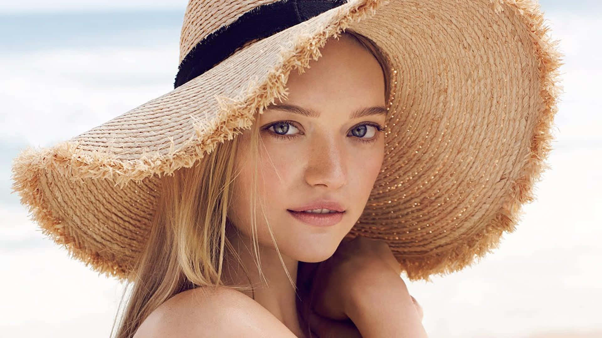 Gemma Ward 桌布 壁紙 — 一位金髮藍眼的年輕女性戴著寬邊草帽，背景是明亮的沙灘。