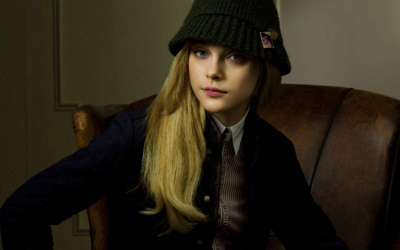jessica stam 桌布 壁紙 — 一位金髮藍眼的年輕女性戴著深綠色無簷便帽，坐在室內的棕色皮革扶手椅上。
