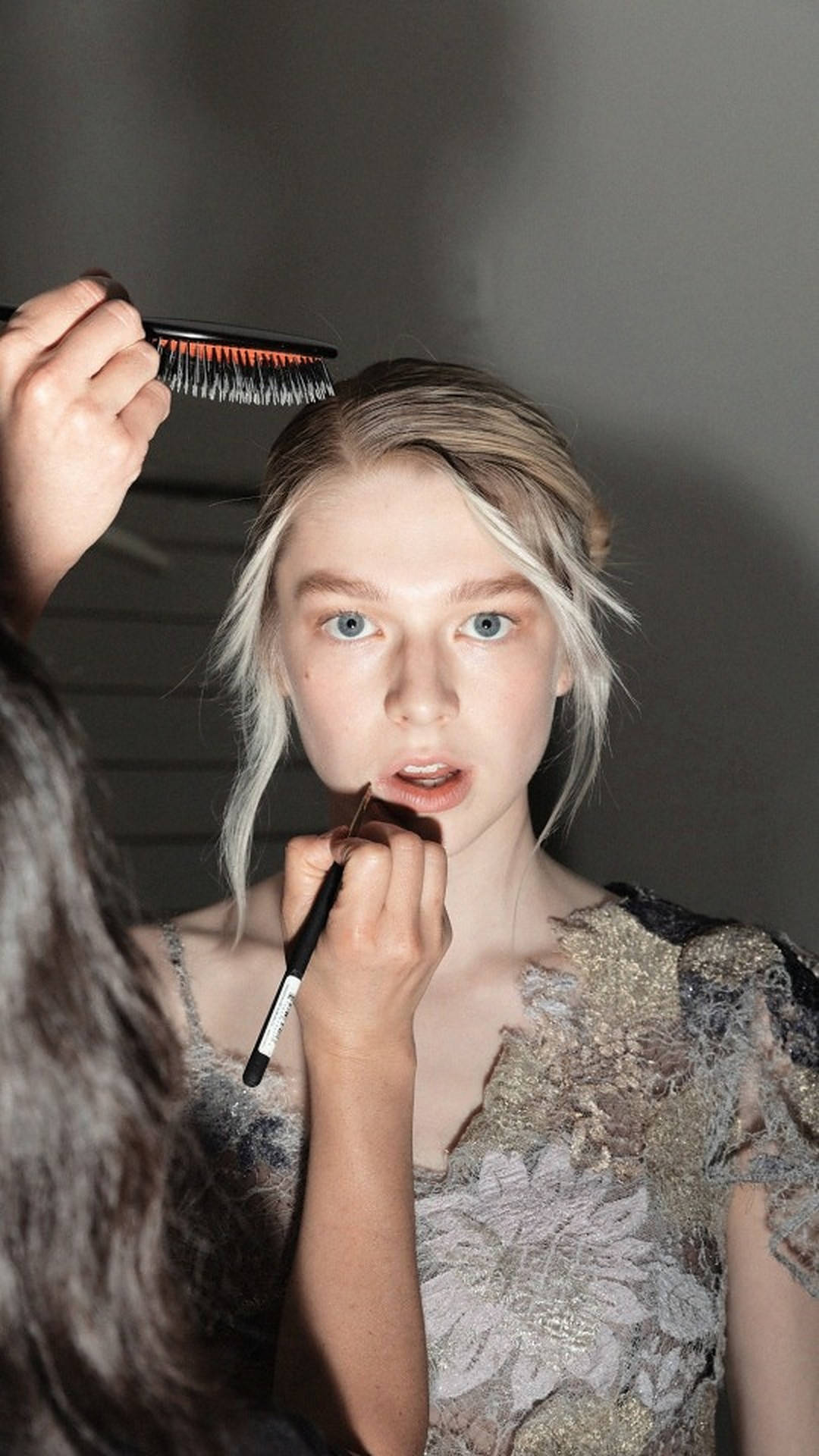 Hunter Schafer 桌布 壁紙 — 一位金髮藍眼的年輕女性正在塗唇膏，同時一把梳子撩起髮絲。