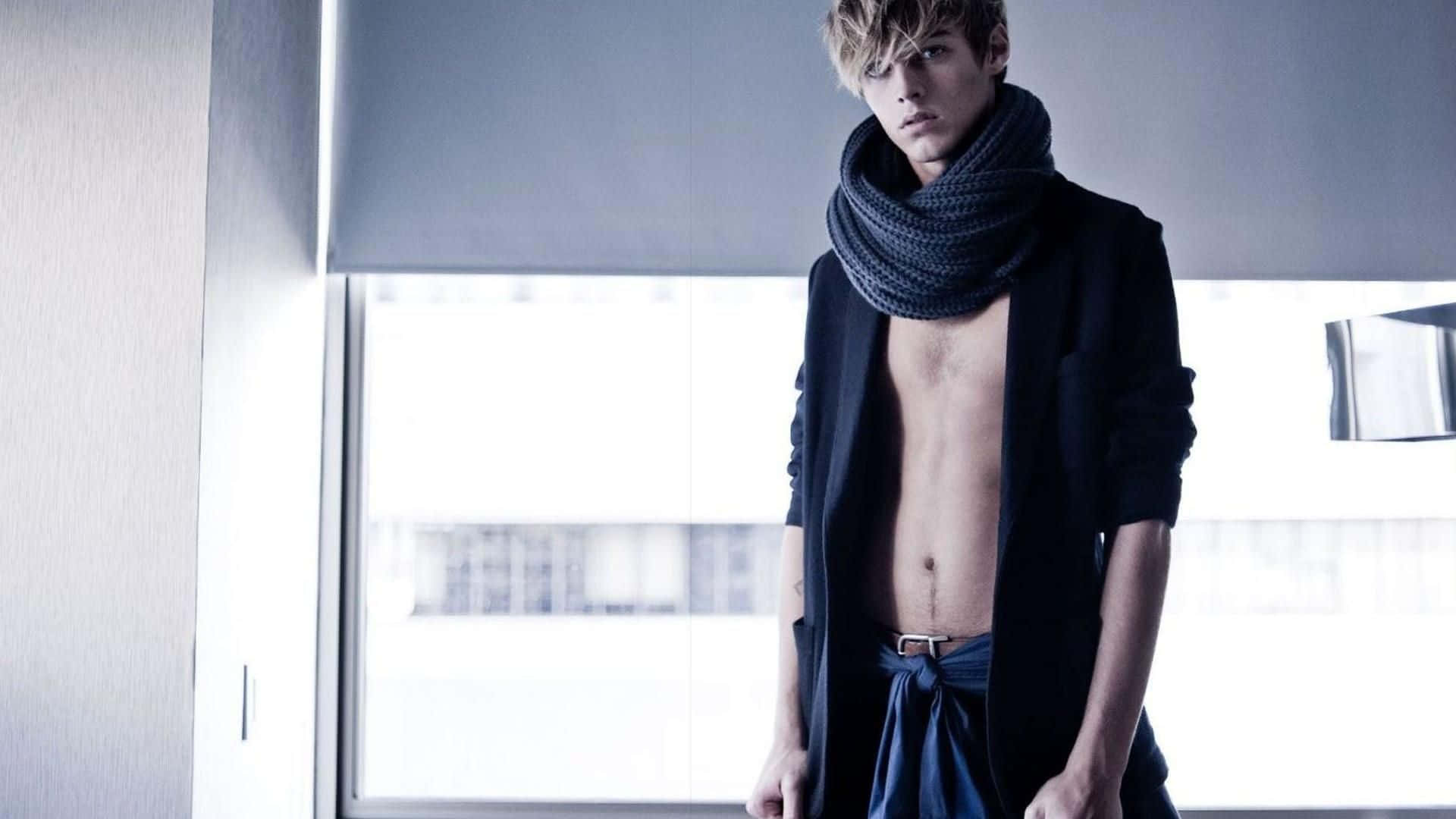 Mens Fashion 桌布 壁紙 — 一位金髮赤膊的年輕男子戴著厚灰色圍巾和敞開的黑色外套，站在現代房間的明亮窗邊。