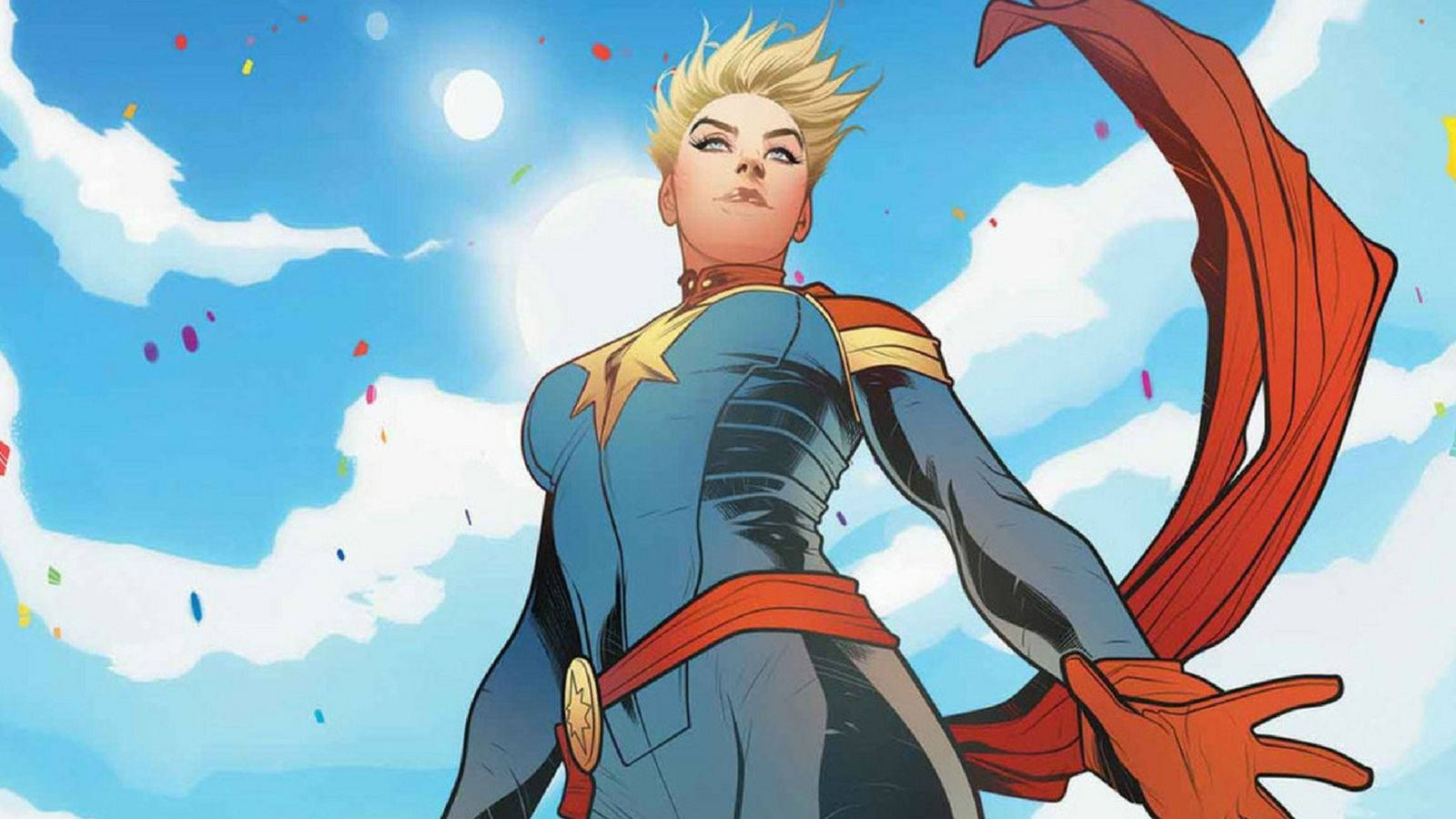 Captain Marvel 桌布 壁紙 — 一位金髮超級英雄身穿藍色套裝和紅色斗篷，自信地站在藍天白雲和彩色紙屑的背景中。