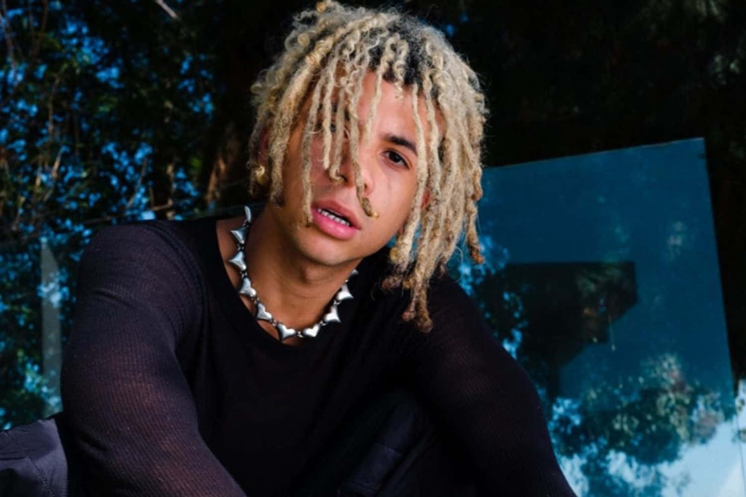 Hip Hop 桌布 壁紙 — 一位金髮辮子、戴著尖刺頸鏈的年輕男子，在深藍色抽象背景前凝視。