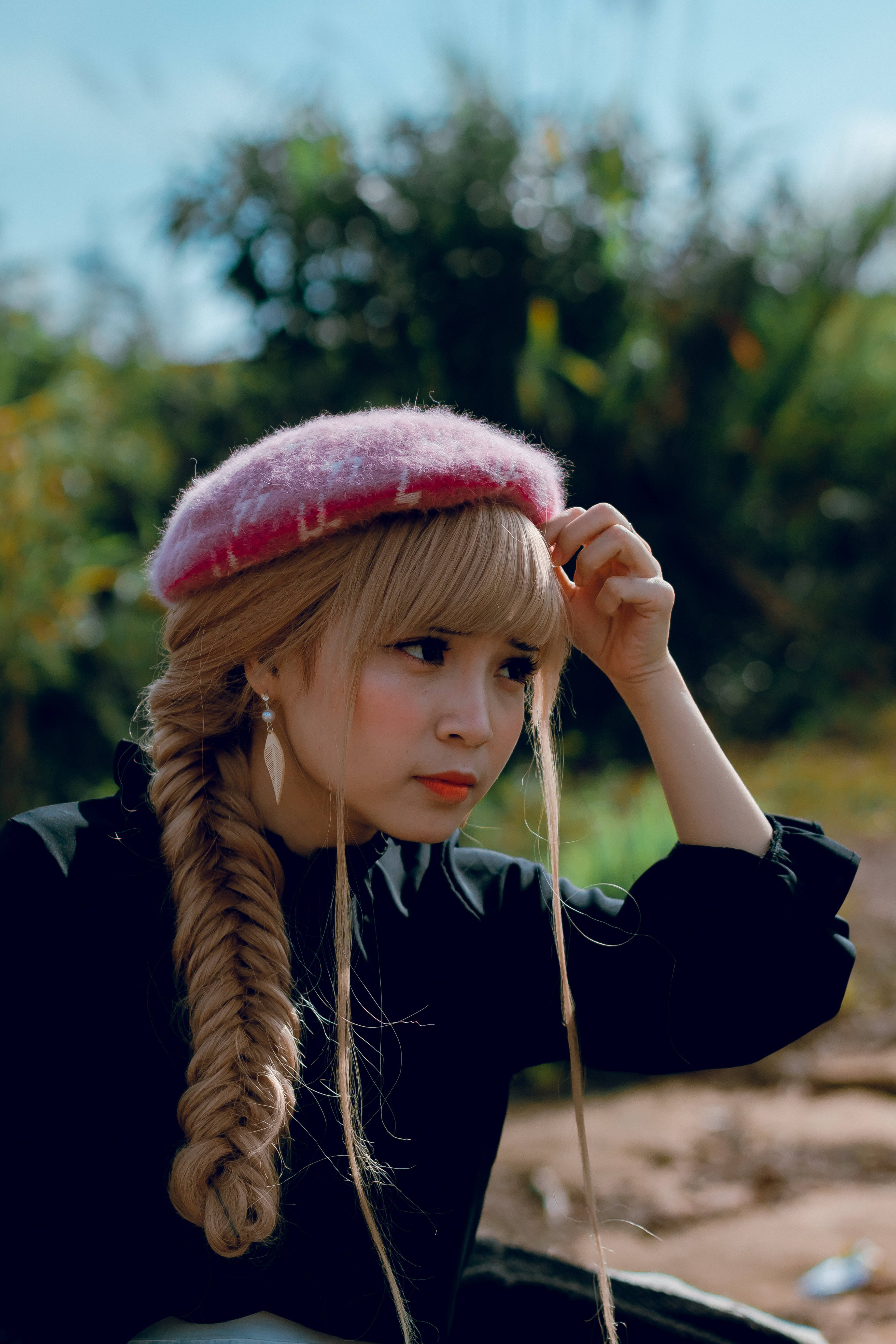 Cute Girl 桌布 壁紙 — 一位金髮辮子、戴著粉紅色貝雷帽的年輕女性，在晴朗的藍天下若有所思地望向戶外。
