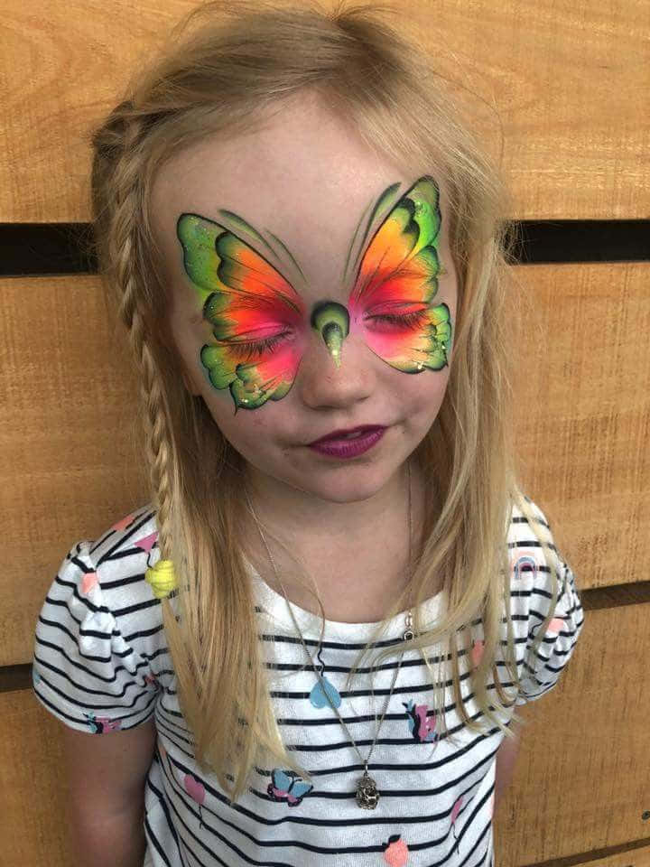 Butterfly Face Painting 桌布 壁紙 — 一位金髮辮子的小女孩溫柔地微笑，臉上畫著的鮮豔蝴蝶翅膀遮住了她的眼睛，背景是木質的。