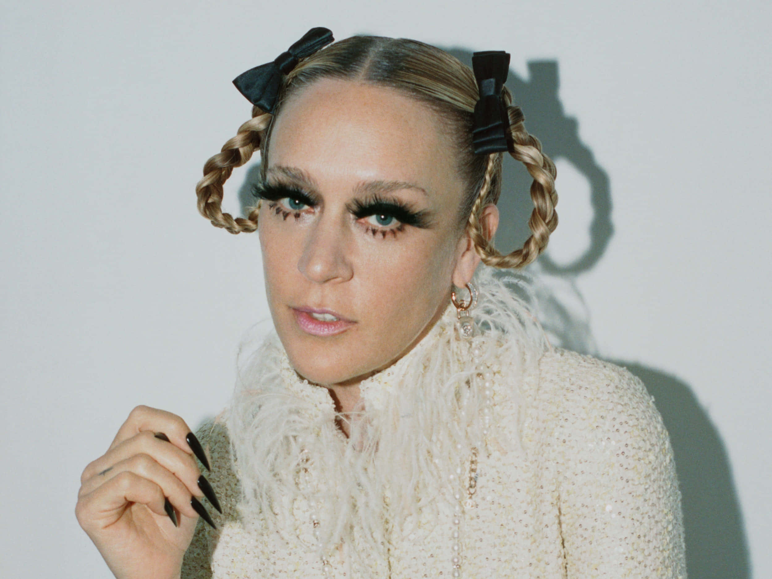 Chloë Sevigny 桌布 壁紙 — 一位金髮辮子頭戴黑色蝴蝶結的女性，穿著蓬鬆的奶油色外套，對著純白牆壁凝視。
