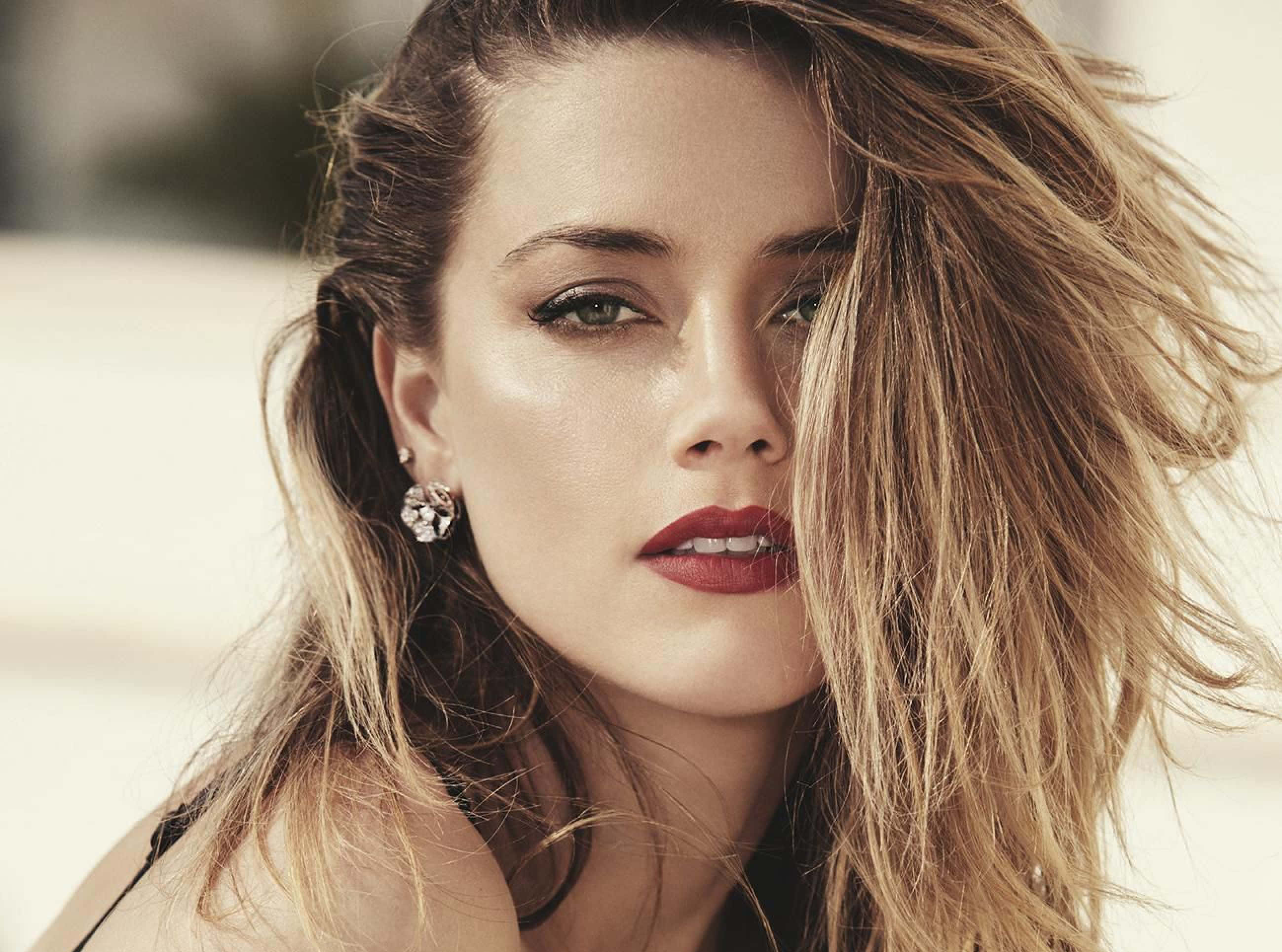 Amber Heard 桌布 壁紙 — 一位金髮隨風飄揚、紅唇大膽的女性在柔和自然光下凝視著相機。