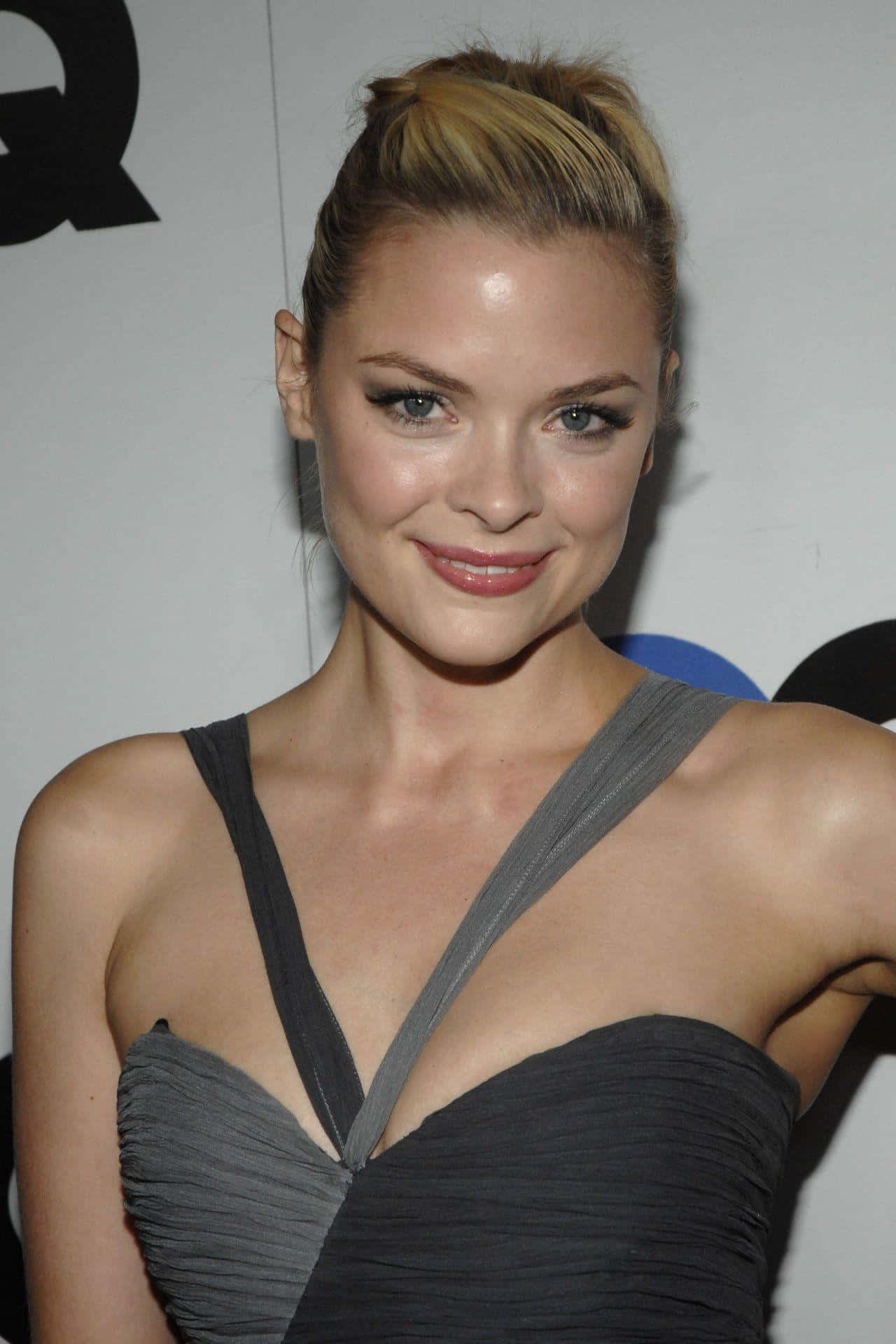 Jaime King 桌布 壁紙 — 一位金髮高髻的女性在活動中穿著灰色百褶裙對著鏡頭微笑。