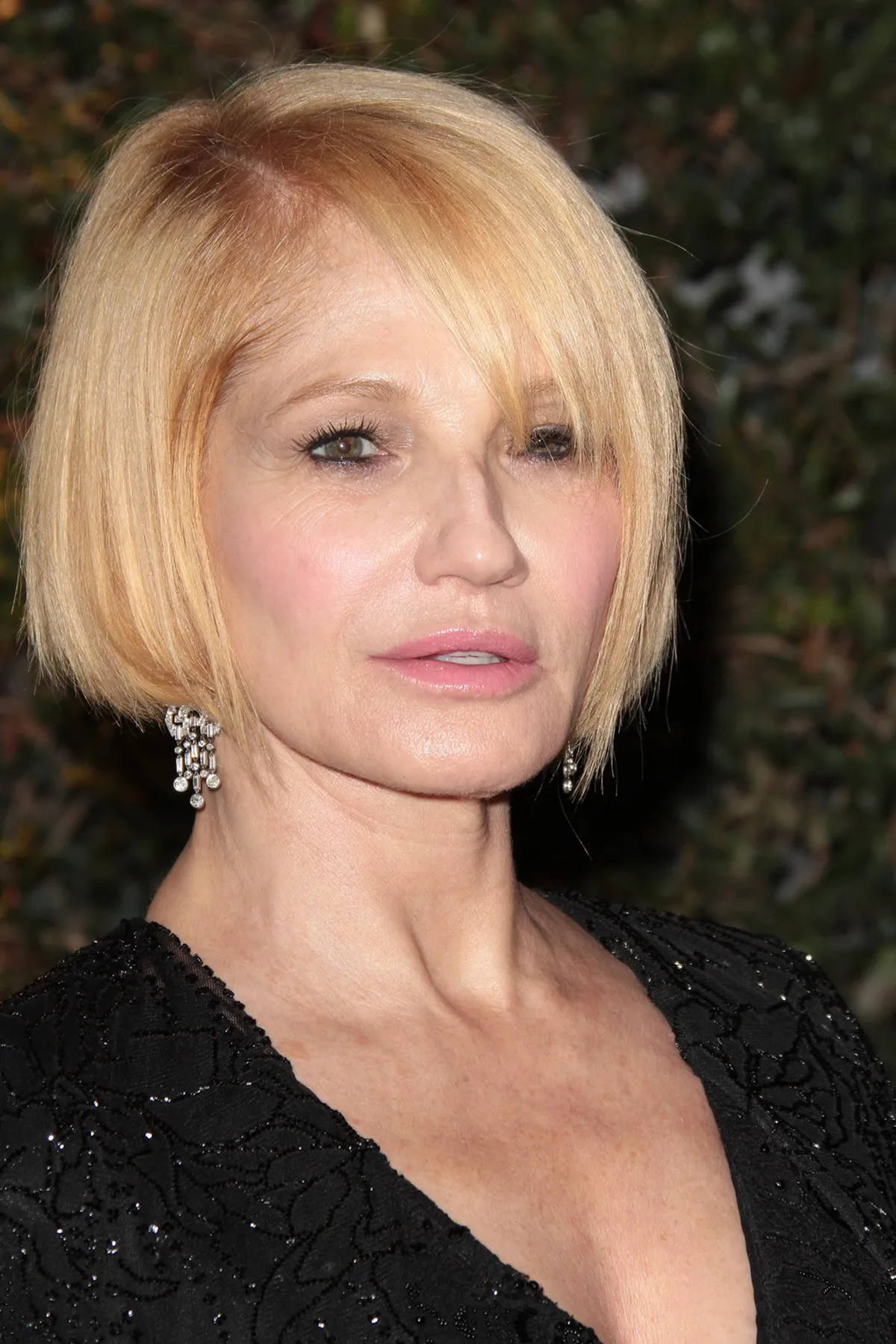 Celebrity 桌布 壁紙 — 一位金髮鮑伯頭女性的特寫肖像，穿著優雅的黑色珠飾連衣裙和垂墜耳環，背景是模糊的綠色樹葉。