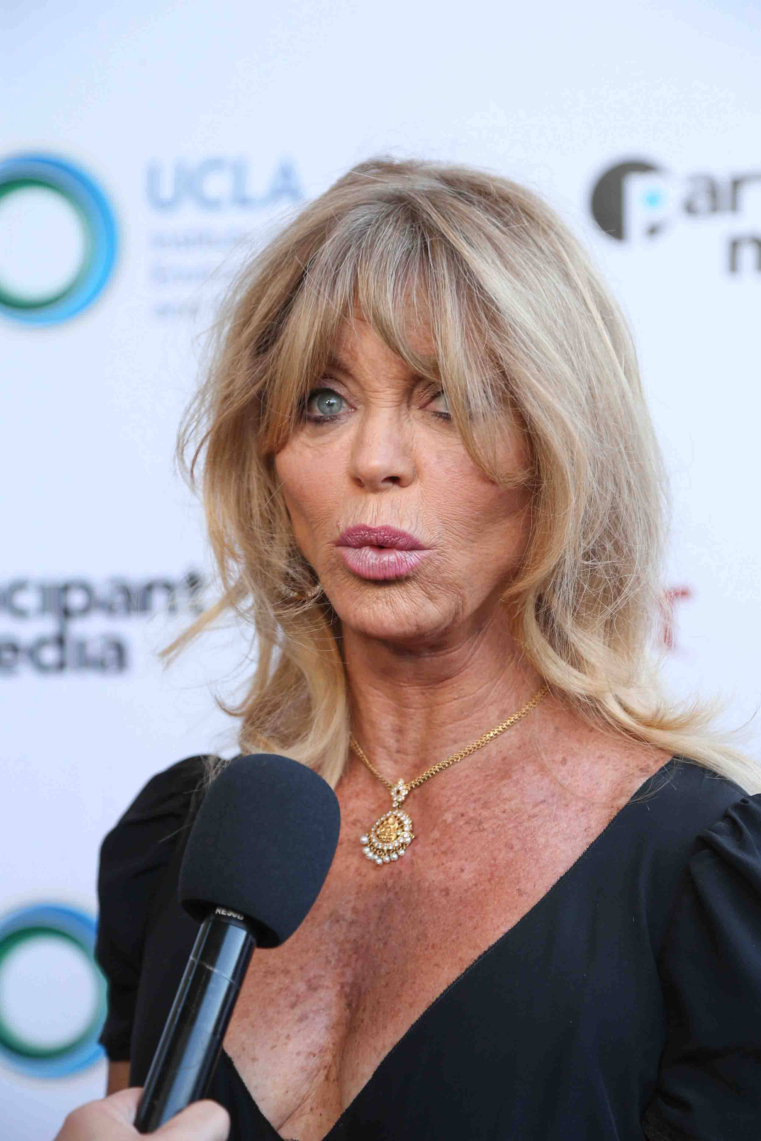 Celebrity 桌布 壁紙 — 一位金髮黑裙的女性在品牌活動背景前對著麥克風講話。