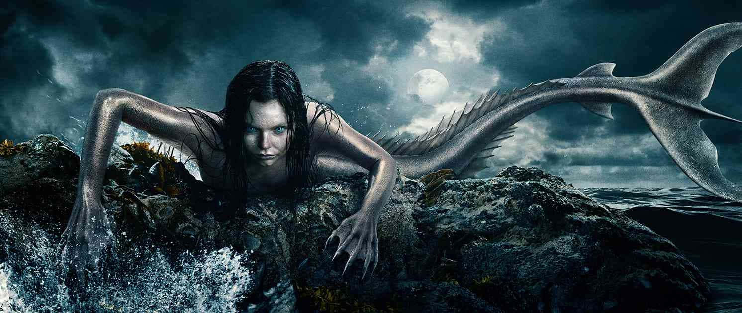 Mermaids 桌布 壁紙 — 一位銀色皮膚、擁有鋒利爪子的美人魚，在月光照耀的暴風雨天空下，從黑暗的海水中浮現到崎嶇的岩石上。