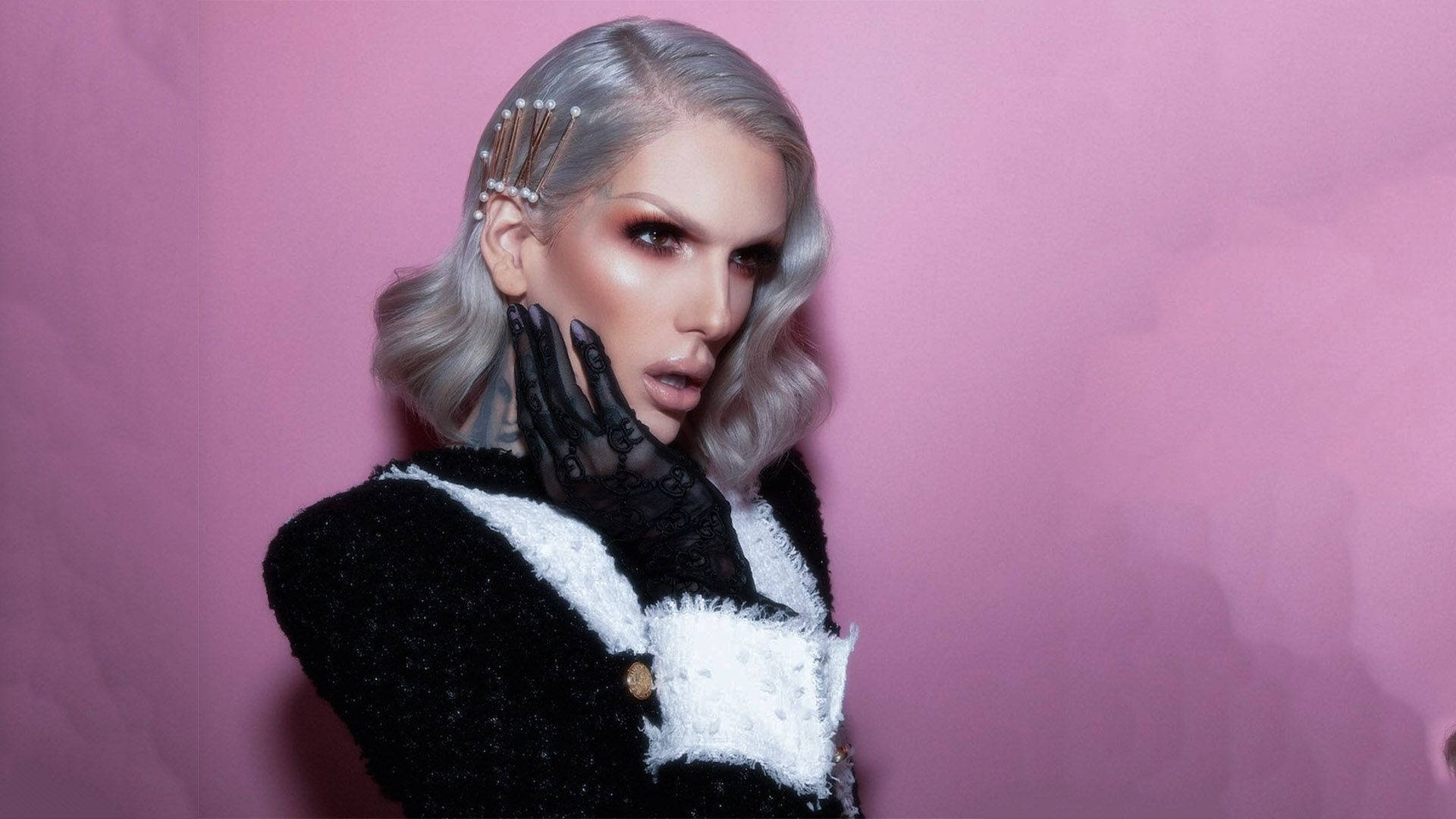 Jeffree Star 桌布 壁紙 — 一位銀髮、妝容大膽的人士，身穿黑白紋理服裝及黑色手套，在粉紅牆前擺姿勢。