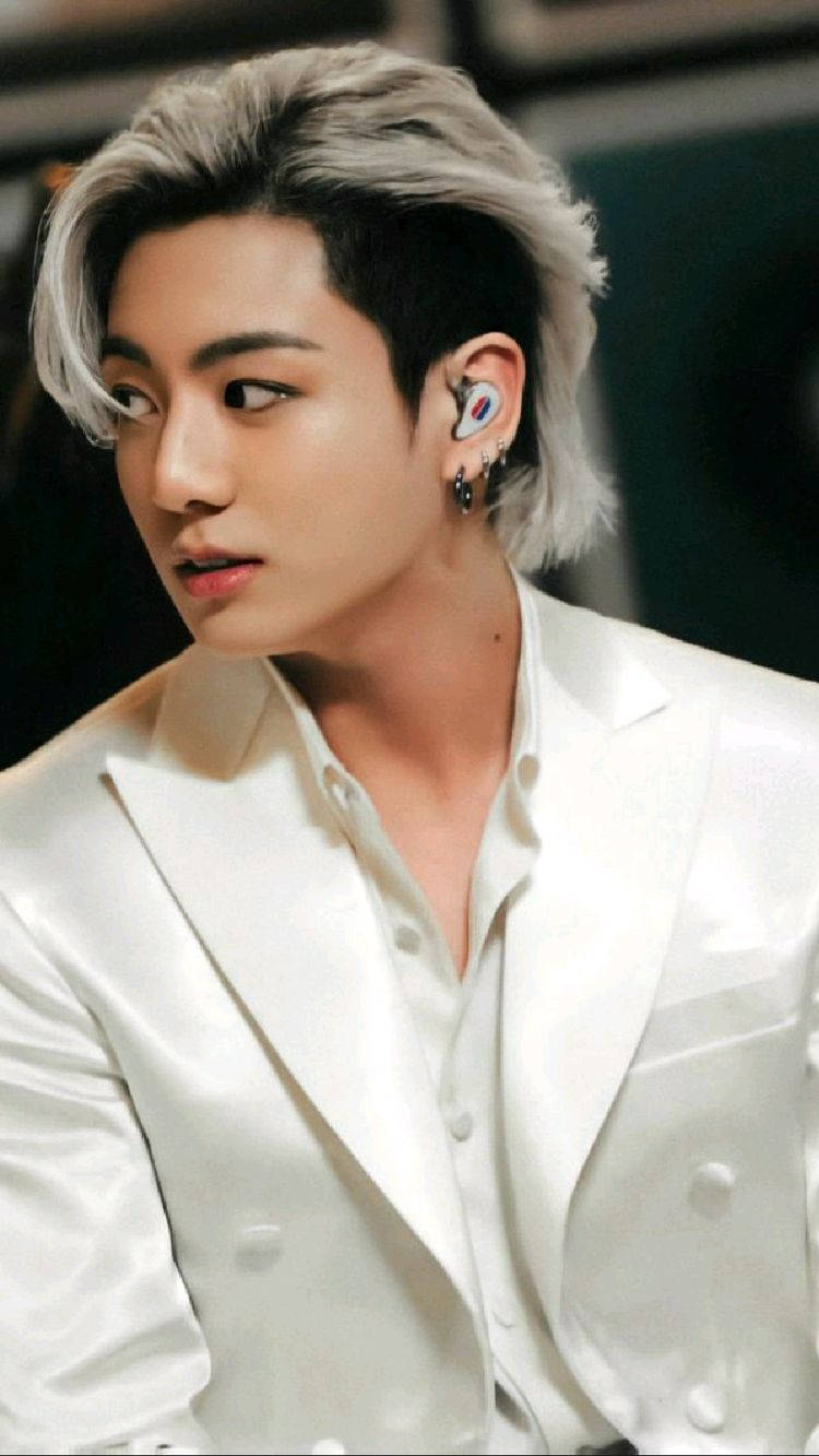 Jungkook 桌布 壁紙 — 一位銀髮、戴著入耳式監聽器的年輕男子，身穿白色緞面西裝外套，表情嚴肅地看向鏡頭外。
