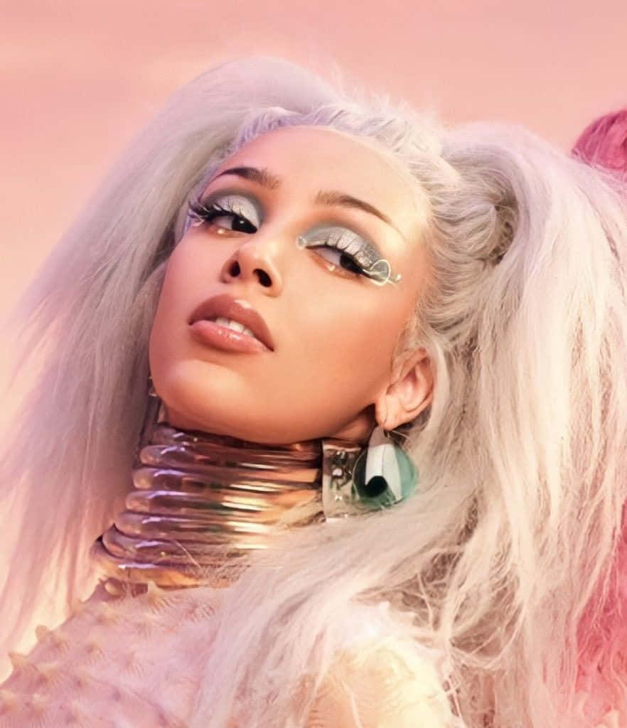 Doja Cat 桌布 壁紙 — 一位銀髮、未來感妝容的迷人女性在柔和的粉紅色天空下擺姿勢。