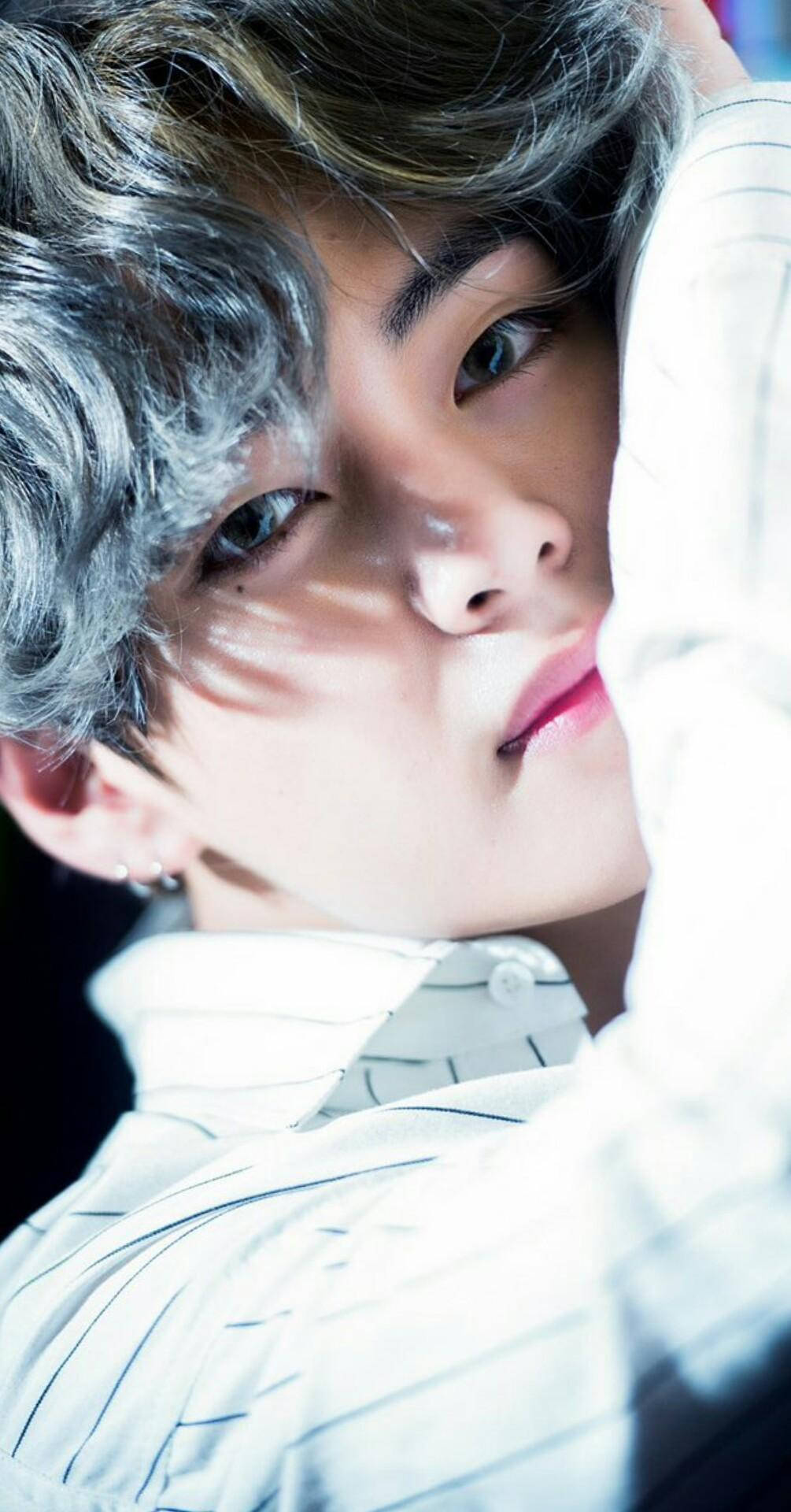 Taehyung Cute 桌布 壁紙 — 一位銀髮、眼神銳利的年輕男子的特寫肖像，身穿白色條紋襯衫，在戲劇性的燈光下照亮。