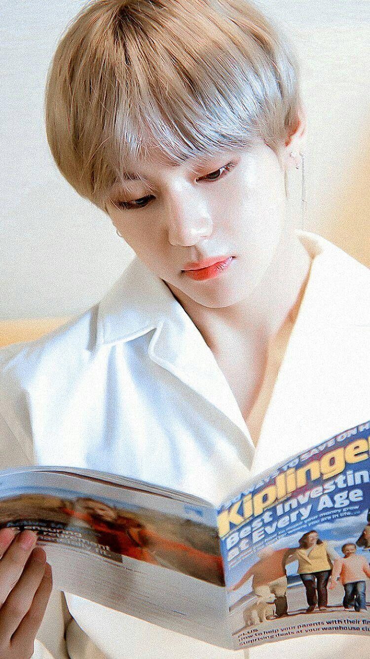 Taehyung Cute 桌布 壁紙 — 一位銀髮年輕人穿著白襯衫，在柔和模糊的背景前專注地閱讀雜誌。