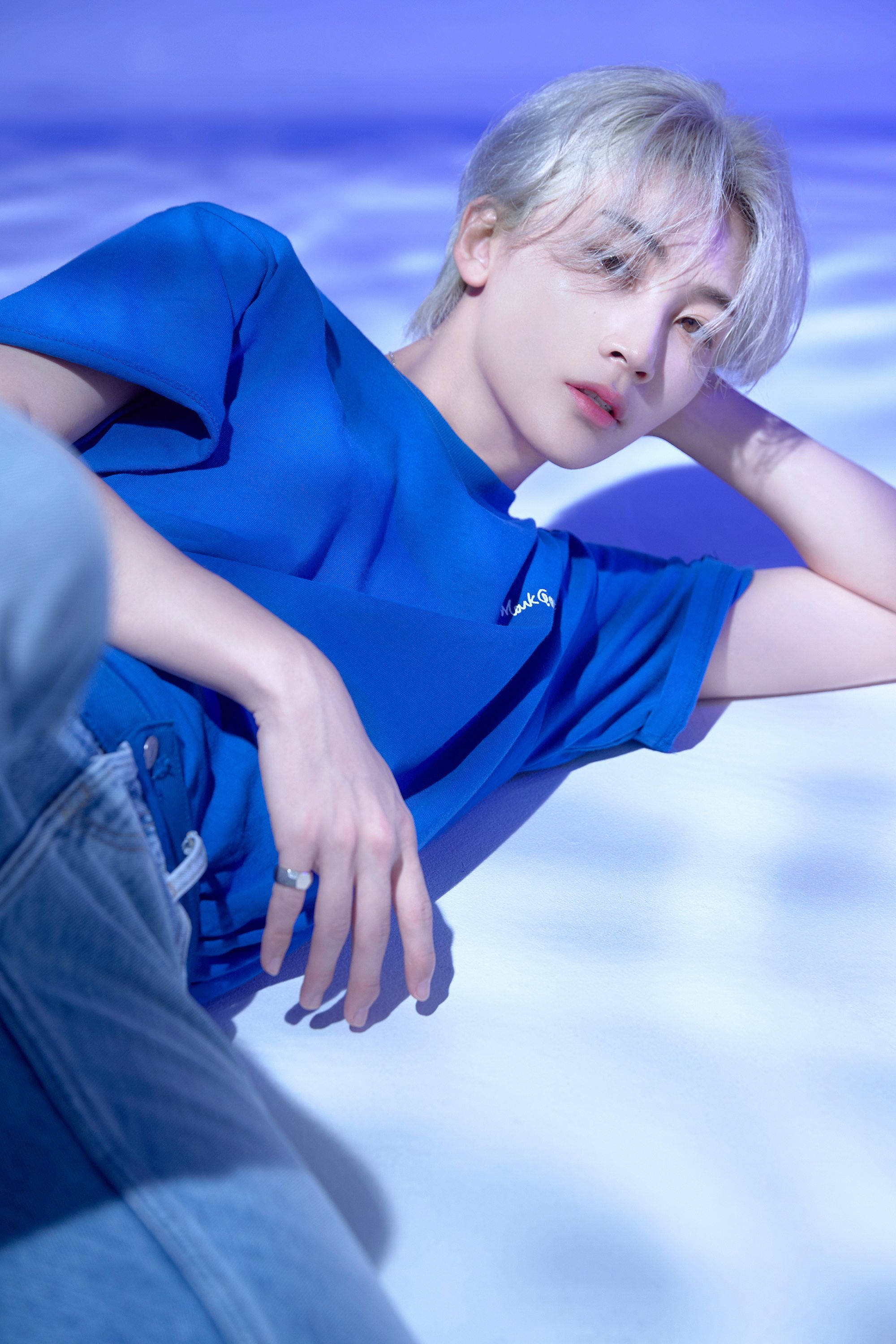 yoon jeonghan 桌布 壁紙 — 一位銀髮年輕人身穿藍色襯衫，在柔和的藍白漸變背景上放鬆。