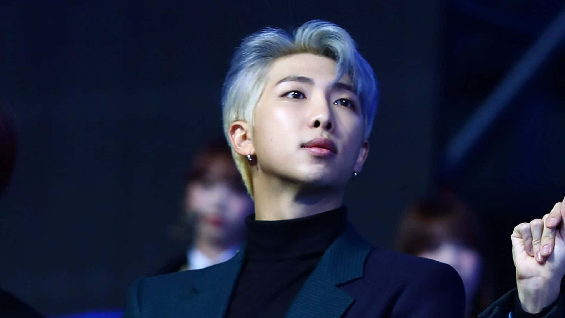 Cute Kpop 桌布 壁紙 — 一位銀髮年輕男子穿著深色西裝，在戲劇性的藍色舞台燈光下向上凝視。