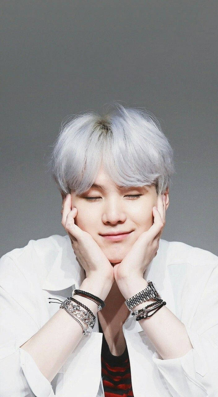 bts iPhone 桌布 壁紙 — 一位銀髮年輕男子閉著眼睛溫柔微笑，雙手捧著臉，背景是純灰色。