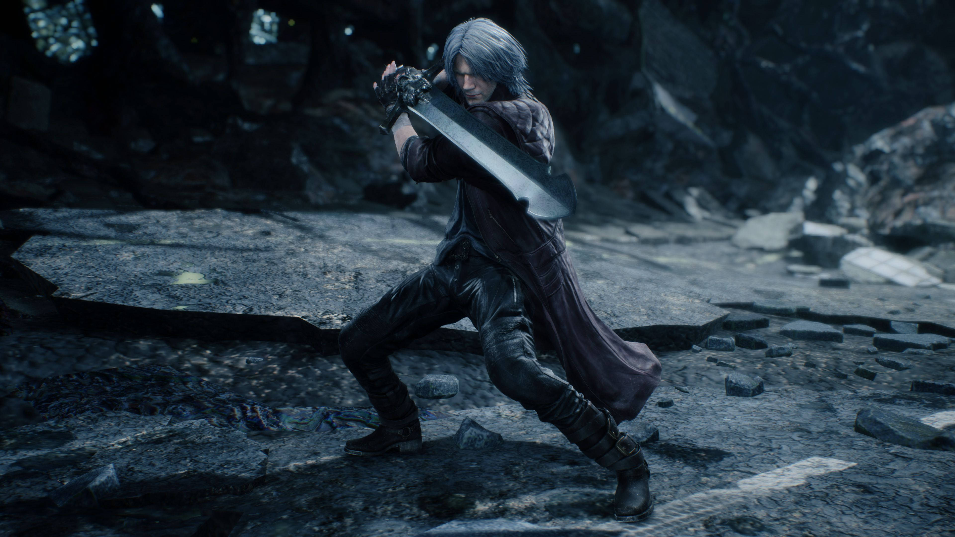 Devil May Cry 5 桌布 壁紙 — 一位銀髮戰士身穿深色服裝，在昏暗燈光下的崎嶇岩石戶外環境中揮舞著一把巨劍。