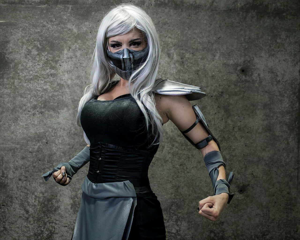 Mortal Kombat Cosplays 桌布 壁紙 — 一位銀髮戴黑色面具的cosplayer，穿著深色盔甲服裝，在粗糙的混凝土牆前擺姿勢。