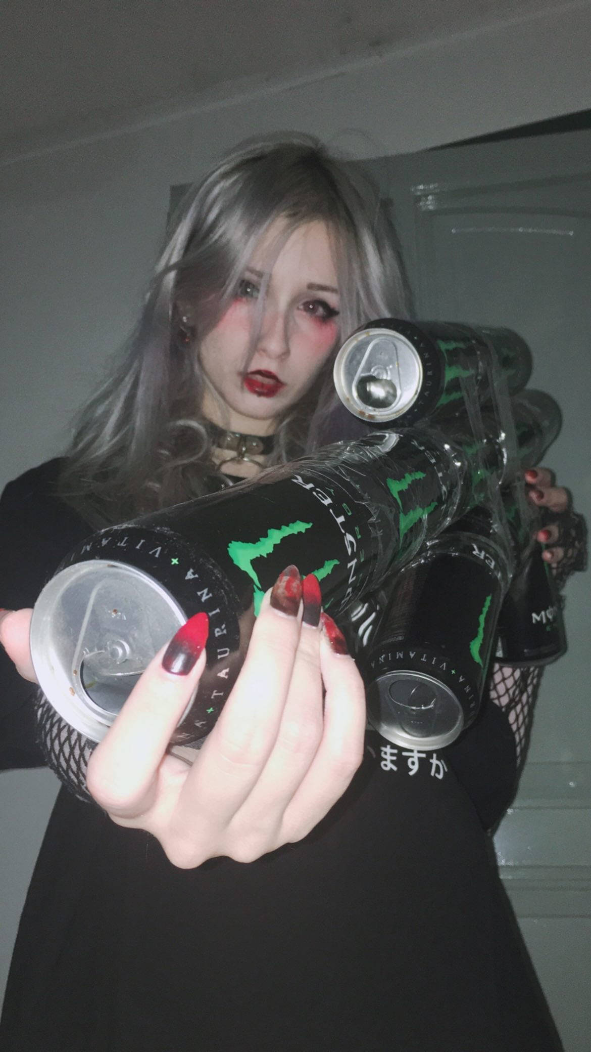Monster Energy 桌布 壁紙 — 一位銀髮紅唇的人士在昏暗的室內環境中手持多罐Monster能量飲料。