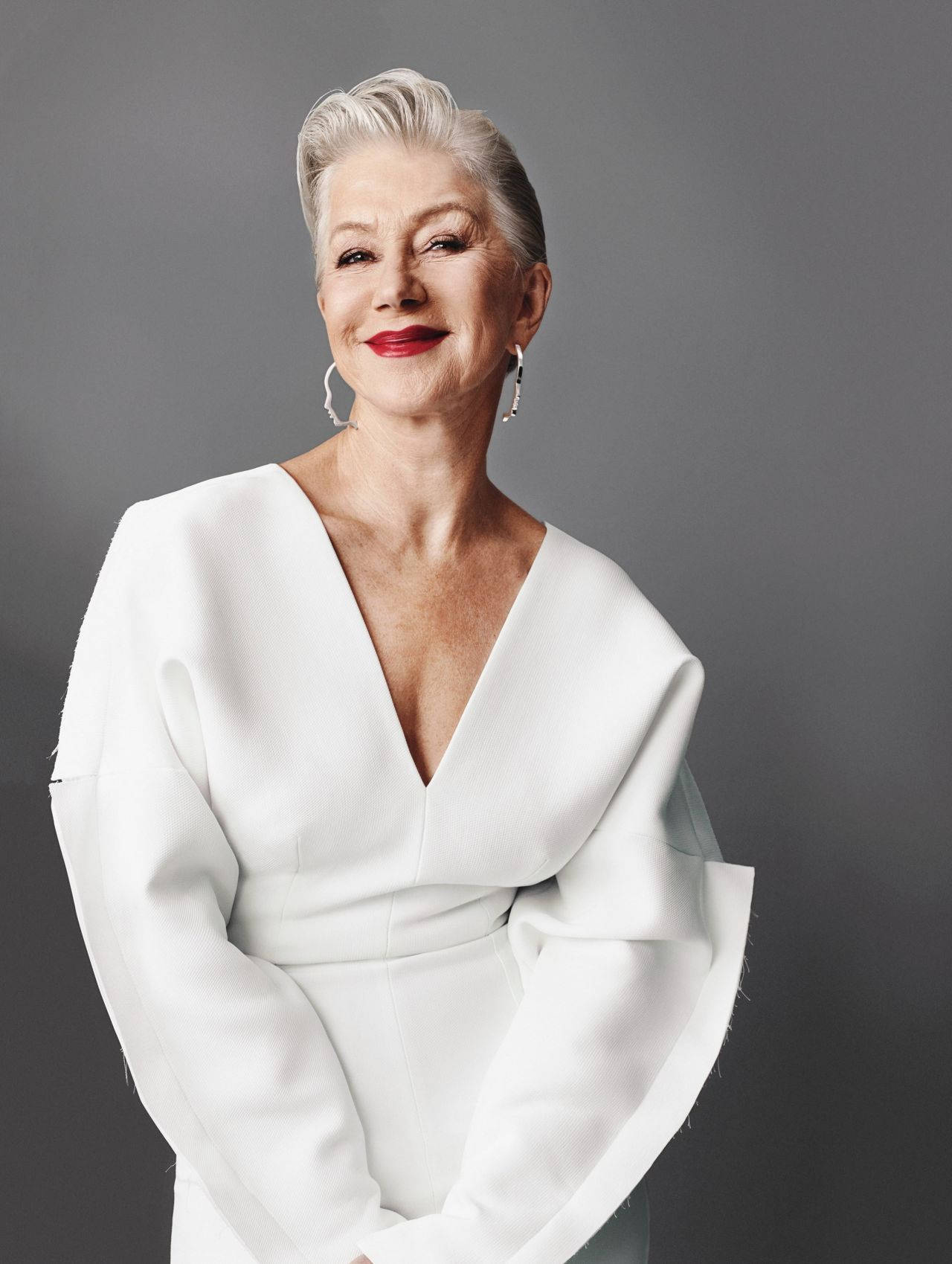 Celebrity 桌布 壁紙 — 一位銀髮紅唇的優雅女性，身穿白色垂褶連衣裙，在灰色背景下溫暖微笑。