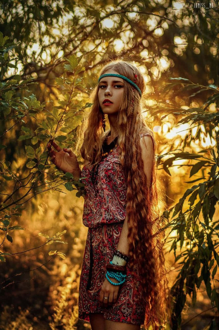 嬉皮 桌布 壁紙 — 一位長捲髮、穿著波希米亞風格服裝的年輕女性，站在陽光灑落的樹林中，沐浴在黃金時刻的溫暖中。