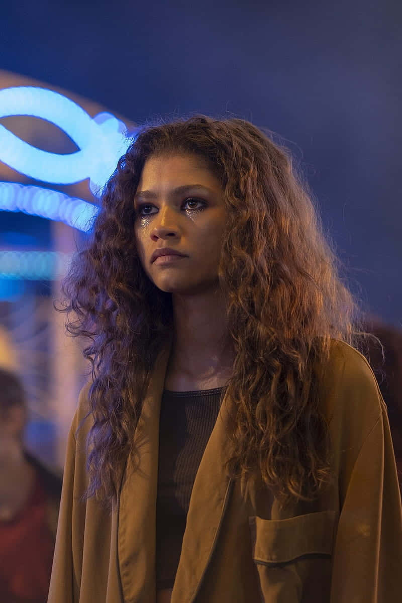 Euphoria Hbo iPhone 桌布 壁紙 — 一位長捲髮女性站在霓虹燈照亮的都市夜景中，臉上帶著淚水，若有所思。