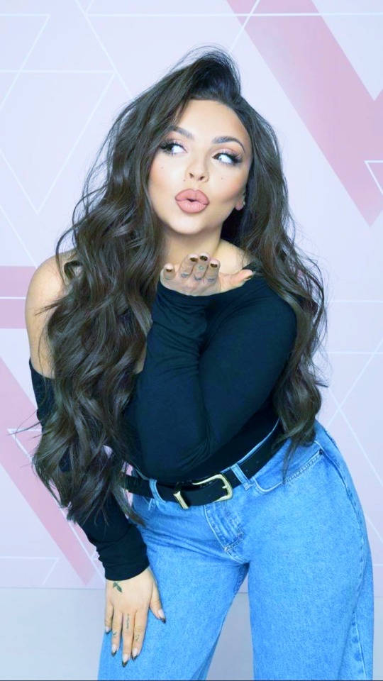 Jesy Nelson 桌布 壁紙 — 一位長捲髮的女性向粉紅色幾何圖案牆壁送飛吻。