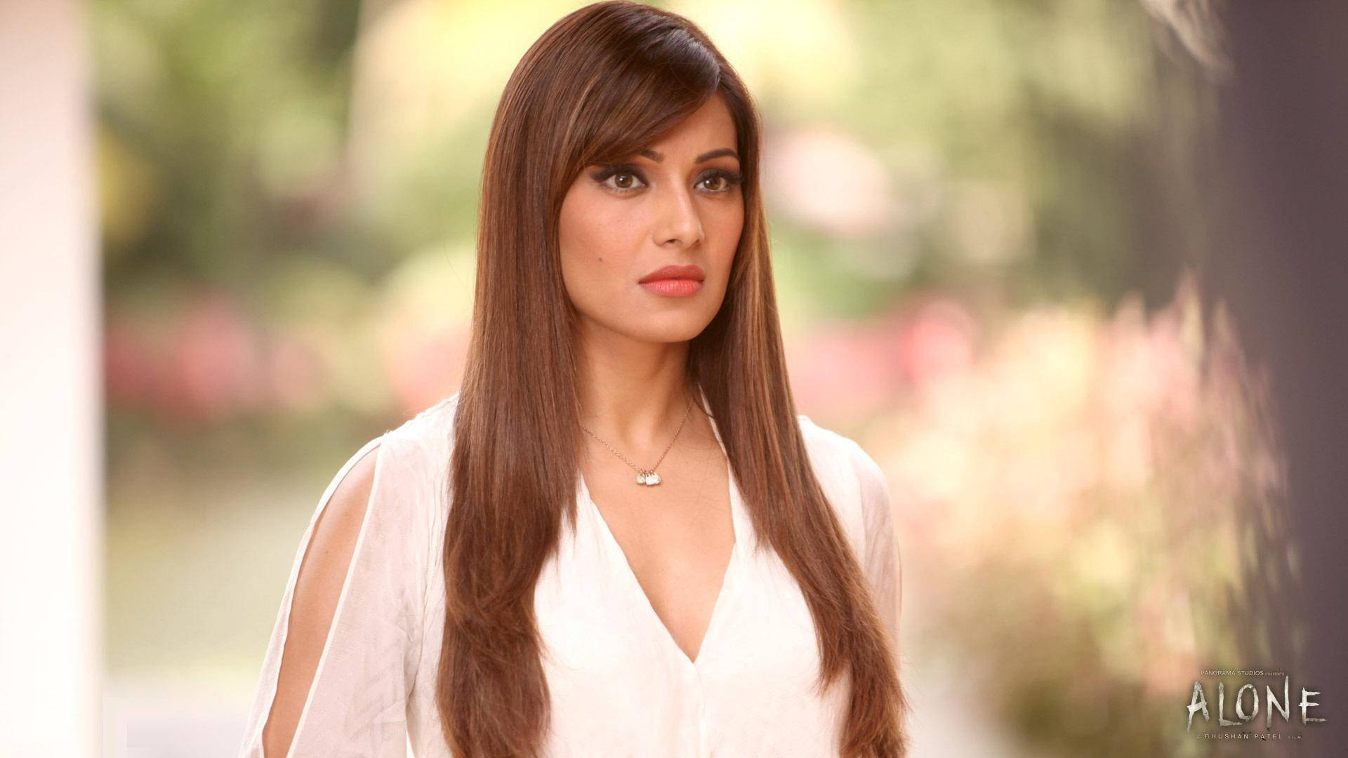 Bipasha Basu 桌布 壁紙 — 一位長棕色頭髮的女性穿著白色襯衫，站在柔和焦點的花園背景中，帶有溫暖的燈光。