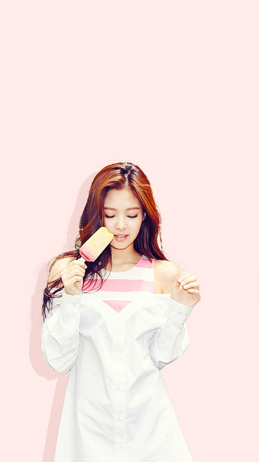 Jennie 桌布 壁紙 — 一位長棕色頭髮的年輕女性在柔和的粉紅色背景前享用粉紅色冰棒。