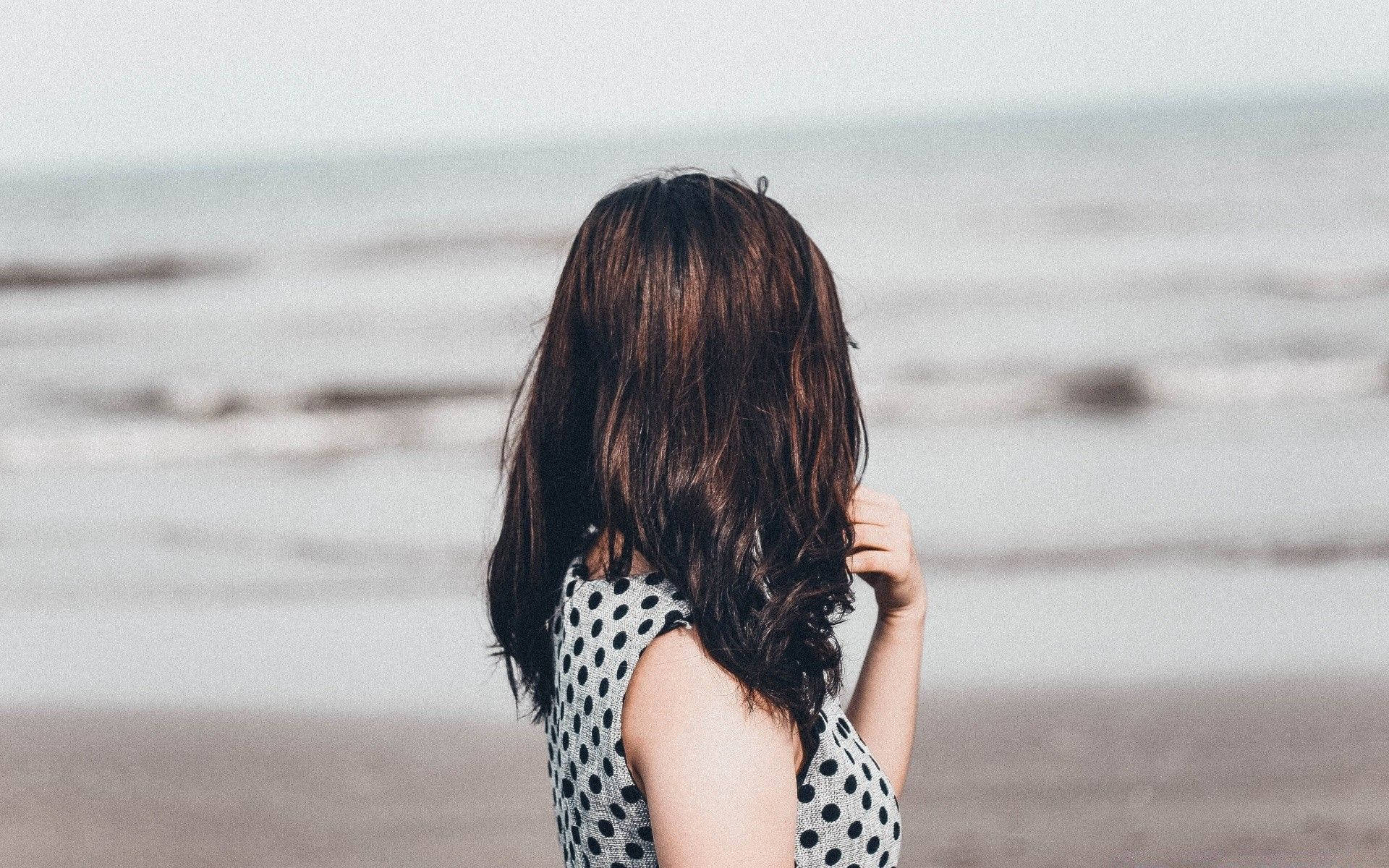 Woman Beautiful 桌布 壁紙 — 一位長棕髮、身穿波點裙的女子站在沙灘上凝視著海浪。