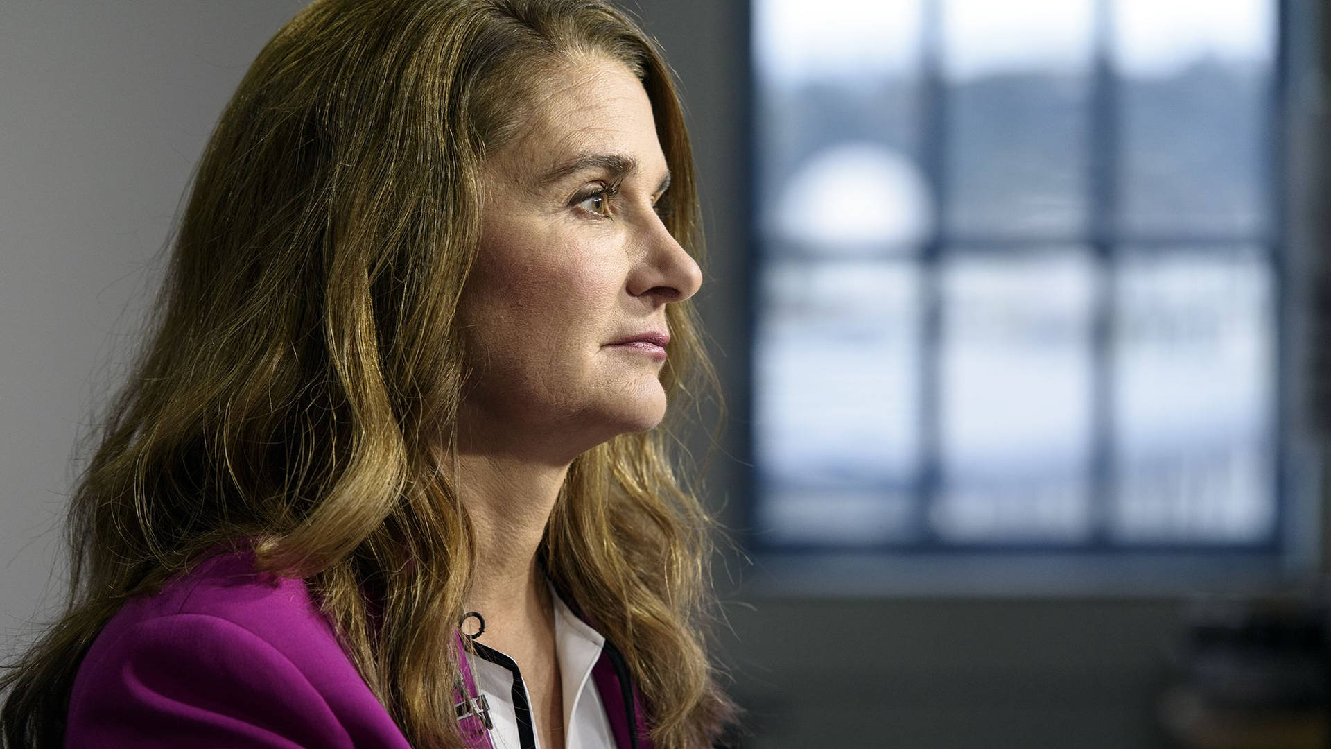 身穿紫色西裝外套的女性在室內望向窗外 — Microsoft 壁紙