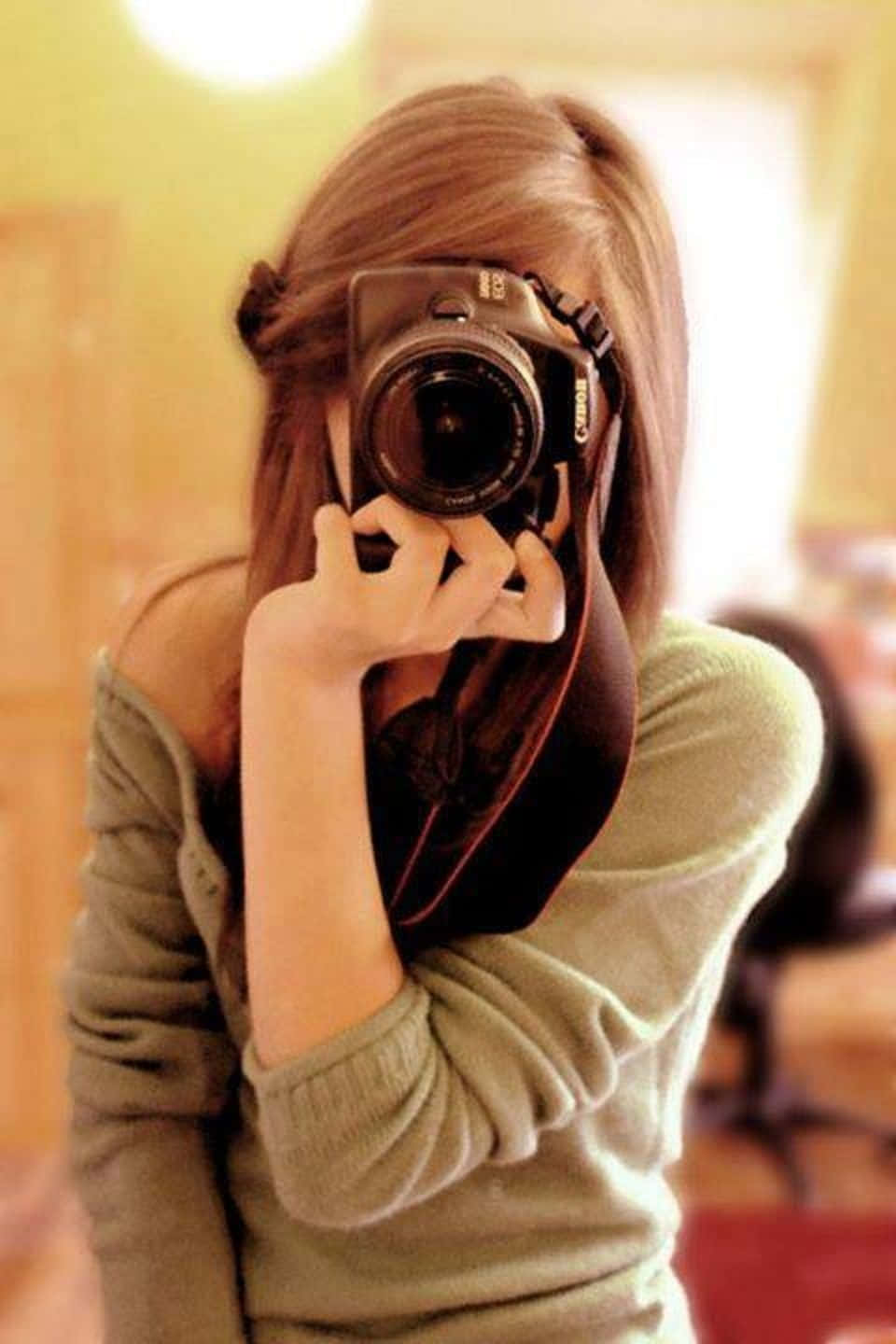 Woman 桌布 壁紙 — 一位長棕髮的人士在鏡子自拍中將Canon相機舉到臉前，穿著綠色毛衣，處於溫暖照明的室內空間。