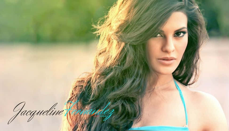 Jacqueline Fernandez 桌布 壁紙 — 一位長波浪髮的女性穿著藍色上衣，在溫暖的金色陽光下直視鏡頭。