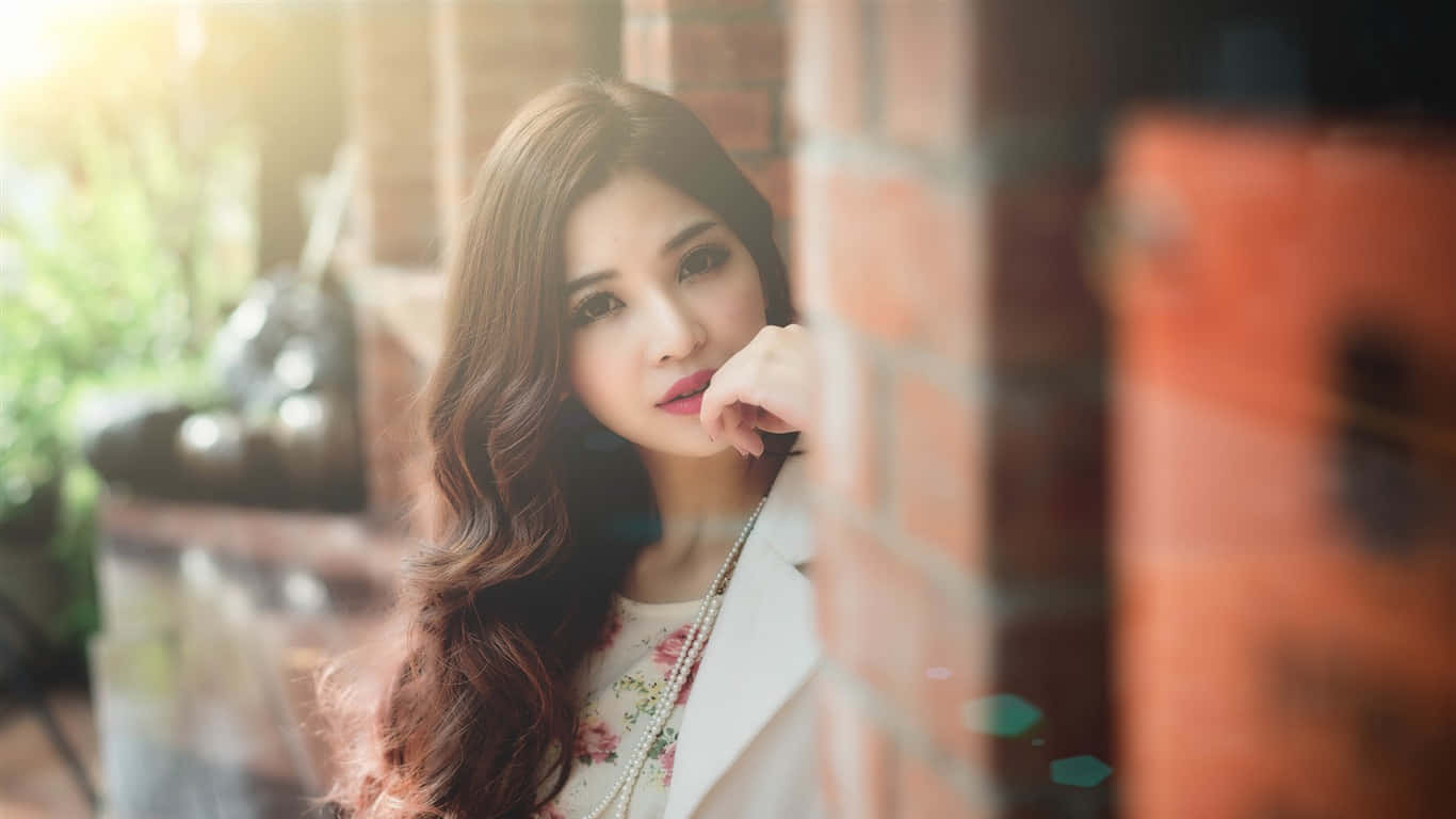 long hair 桌布 壁紙 — 一位長波浪髮的年輕女子靠著磚牆，溫暖的陽光從她身後透進來。