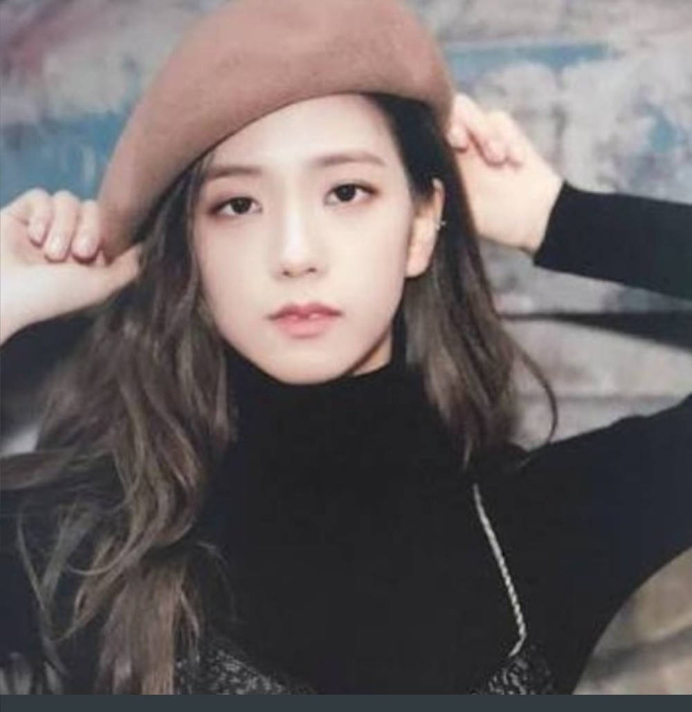 Jisoo Cute 桌布 壁紙 — 一位長波浪髮的年輕女性戴著棕色貝雷帽和黑色高領毛衣，在紋理牆壁背景前調整帽子。