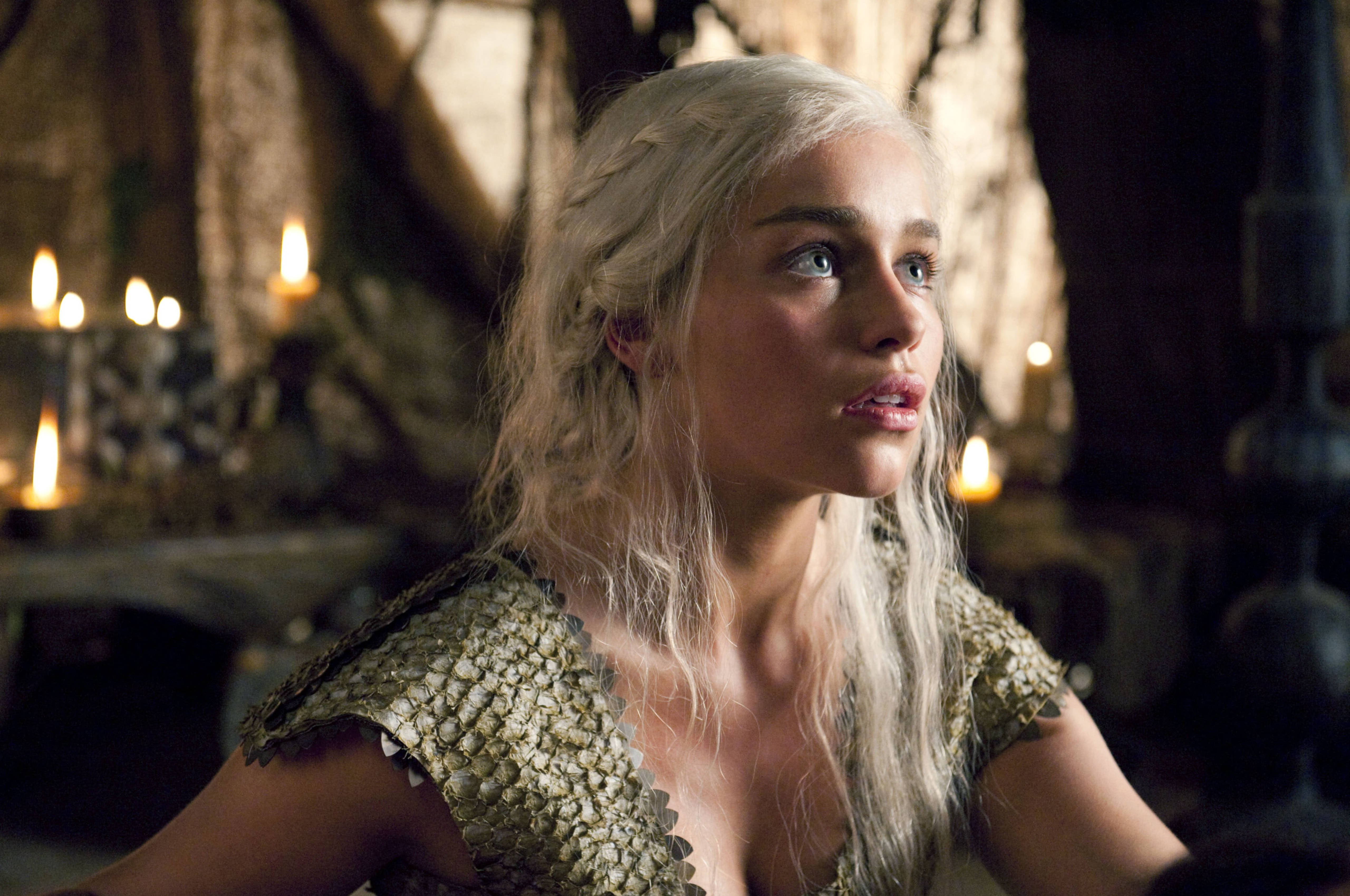 daenerys 桌布 壁紙 — 一位長白髮女子身穿金色鱗片狀連衣裙，在燭光中世紀大廳中向上凝視。